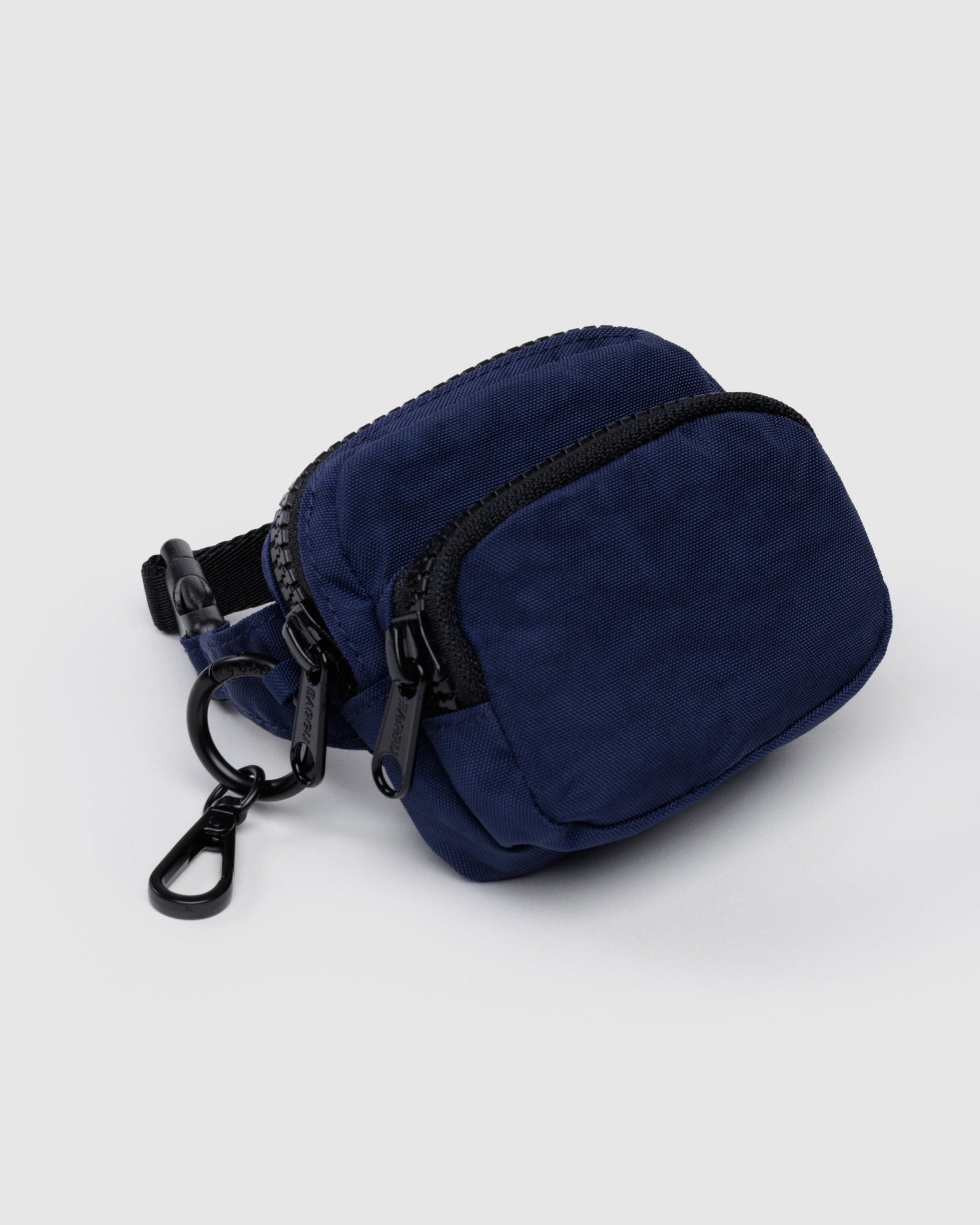 Small, navy blue fanny charm with black zippers on two pockets, a clip and black adjustable strap