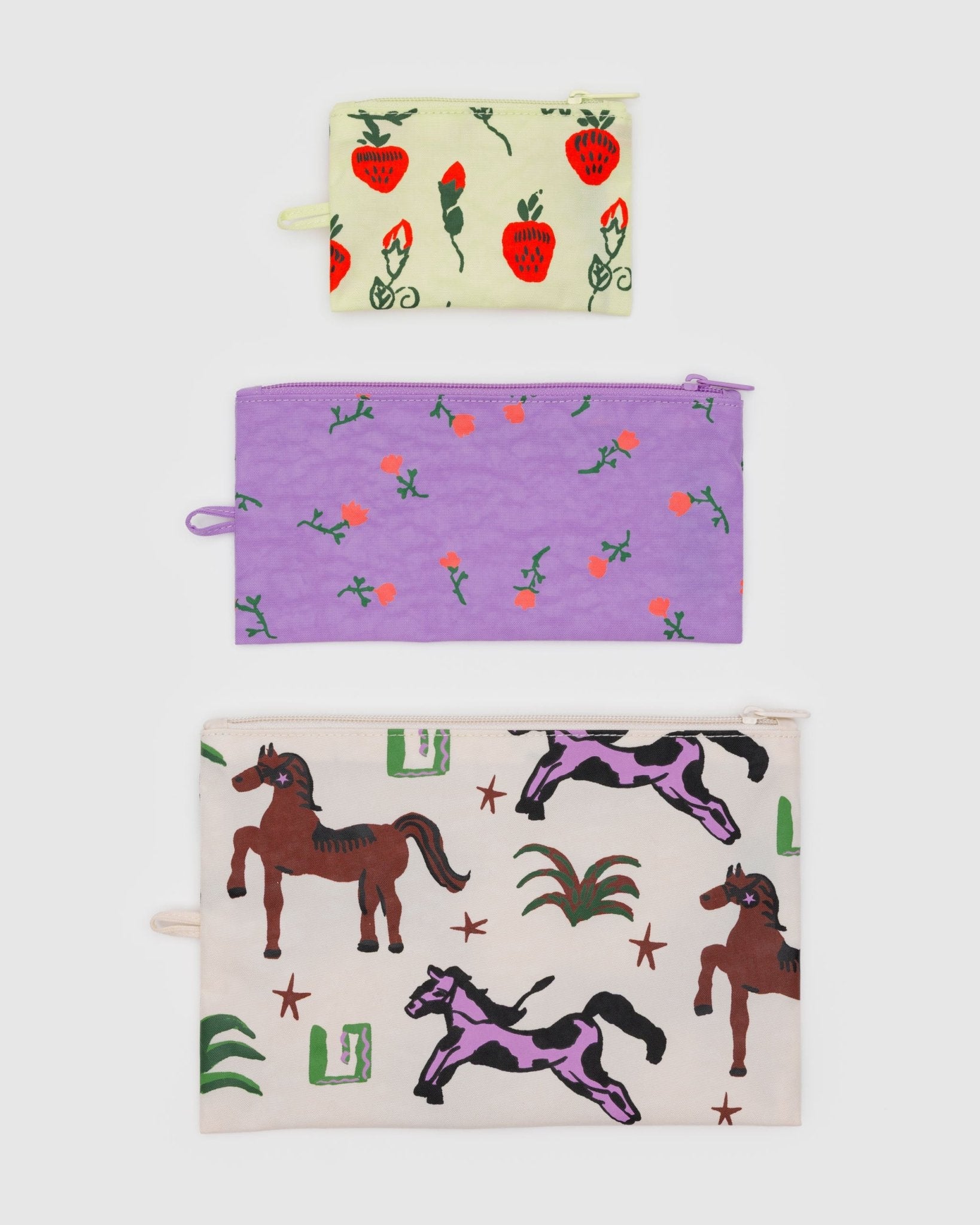 Three different sized pouches with keychain loop at side each in a different pattern of strawberries, horses and wildflowers