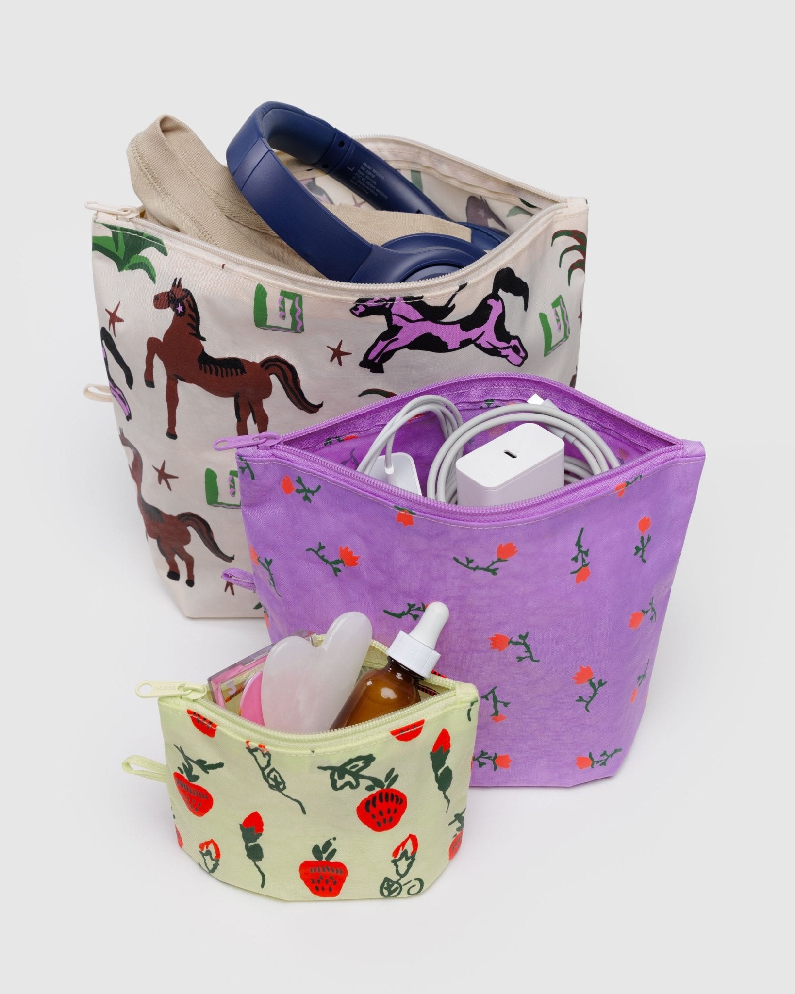 Three different sized pouches with different patterns of strawberries, flowers and horses filled with contents