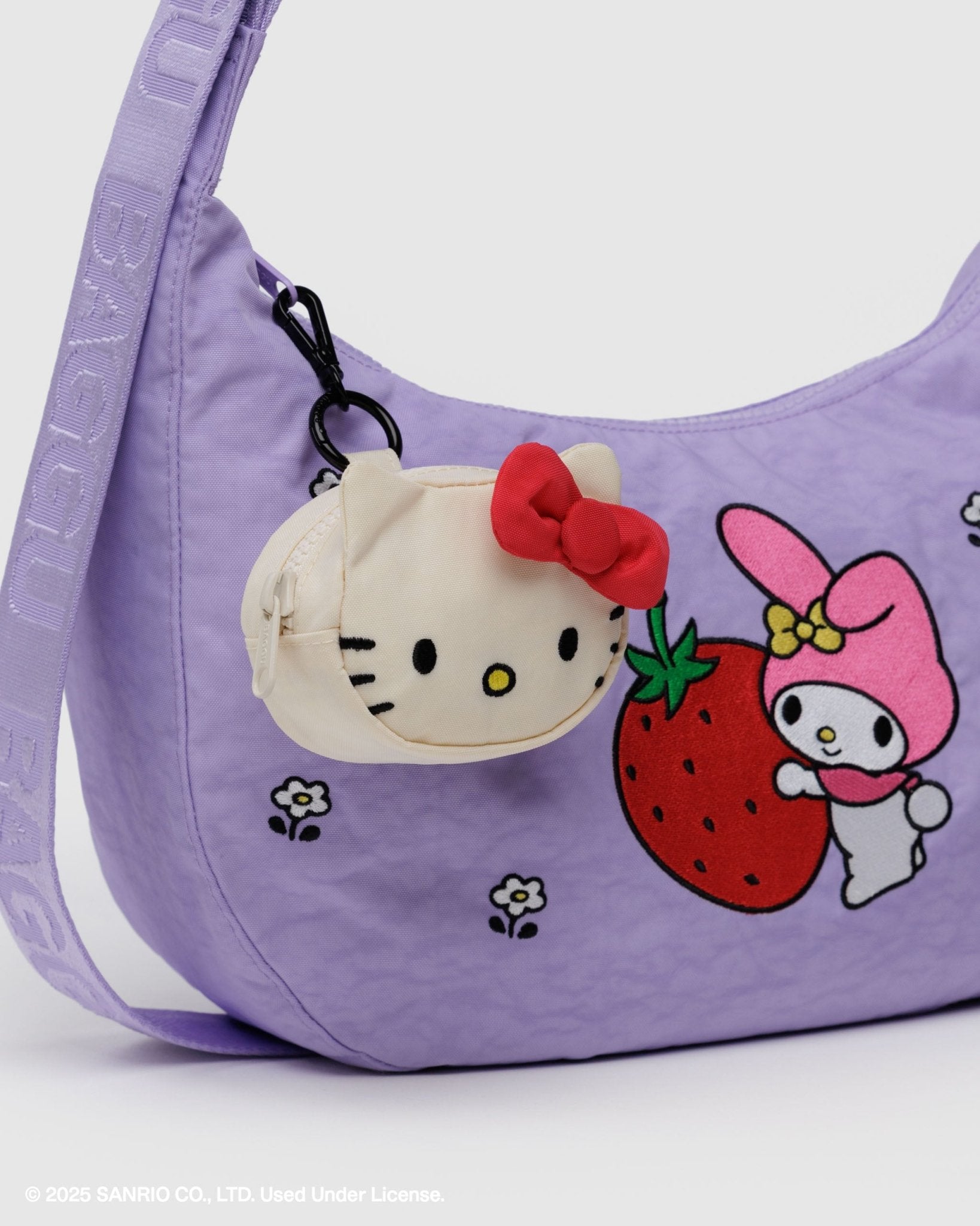White kitty face with ears on round charm bag with red bow attached, zip top and carabiner attached to zip of purple handbag