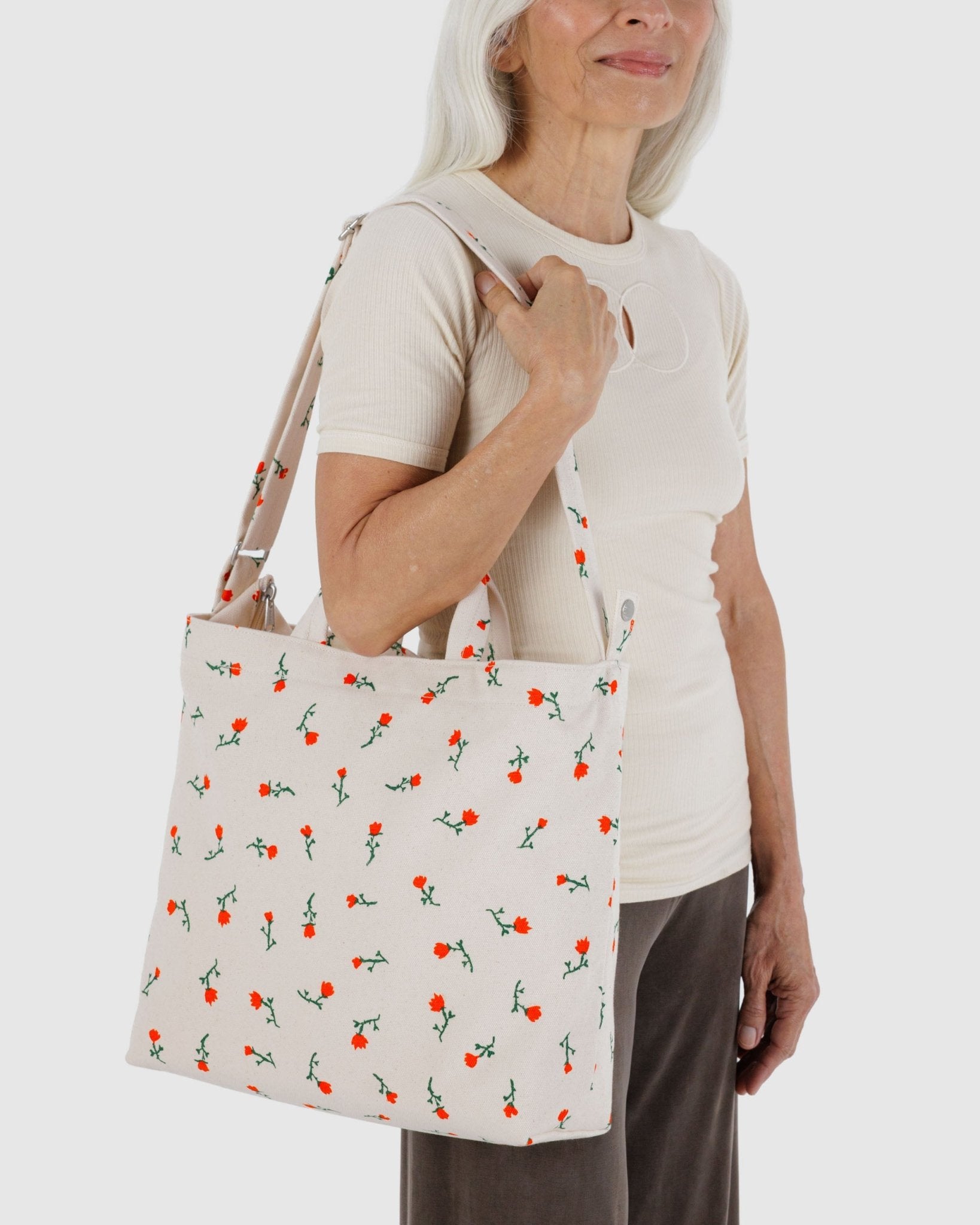 Woman holding a white tote bag with red wildflowers pattern on shoulder with adjustable strap