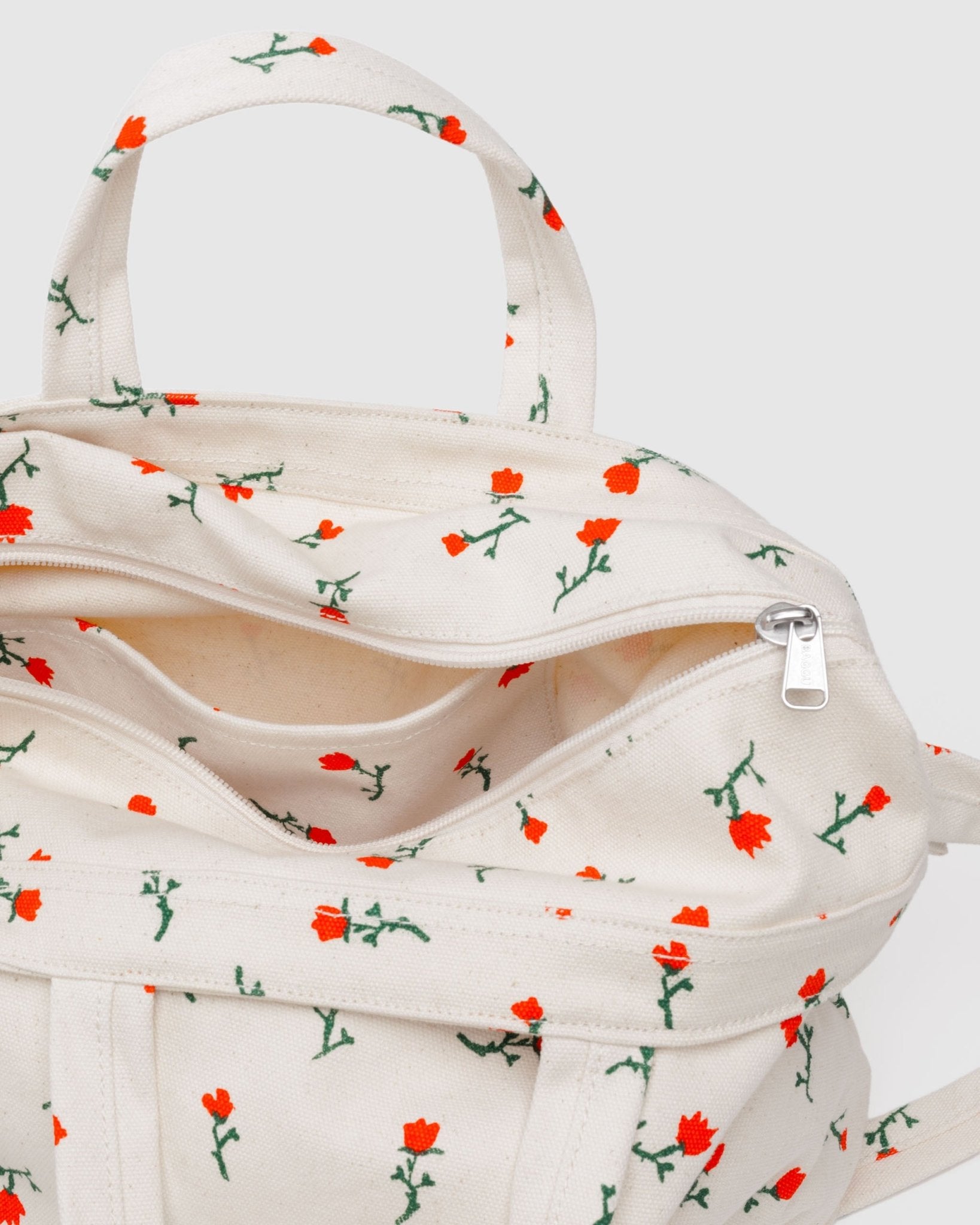White tote bag with red wilflowers pattern, an adjustable strap and carry handles, an internal pocket and zip top closure
