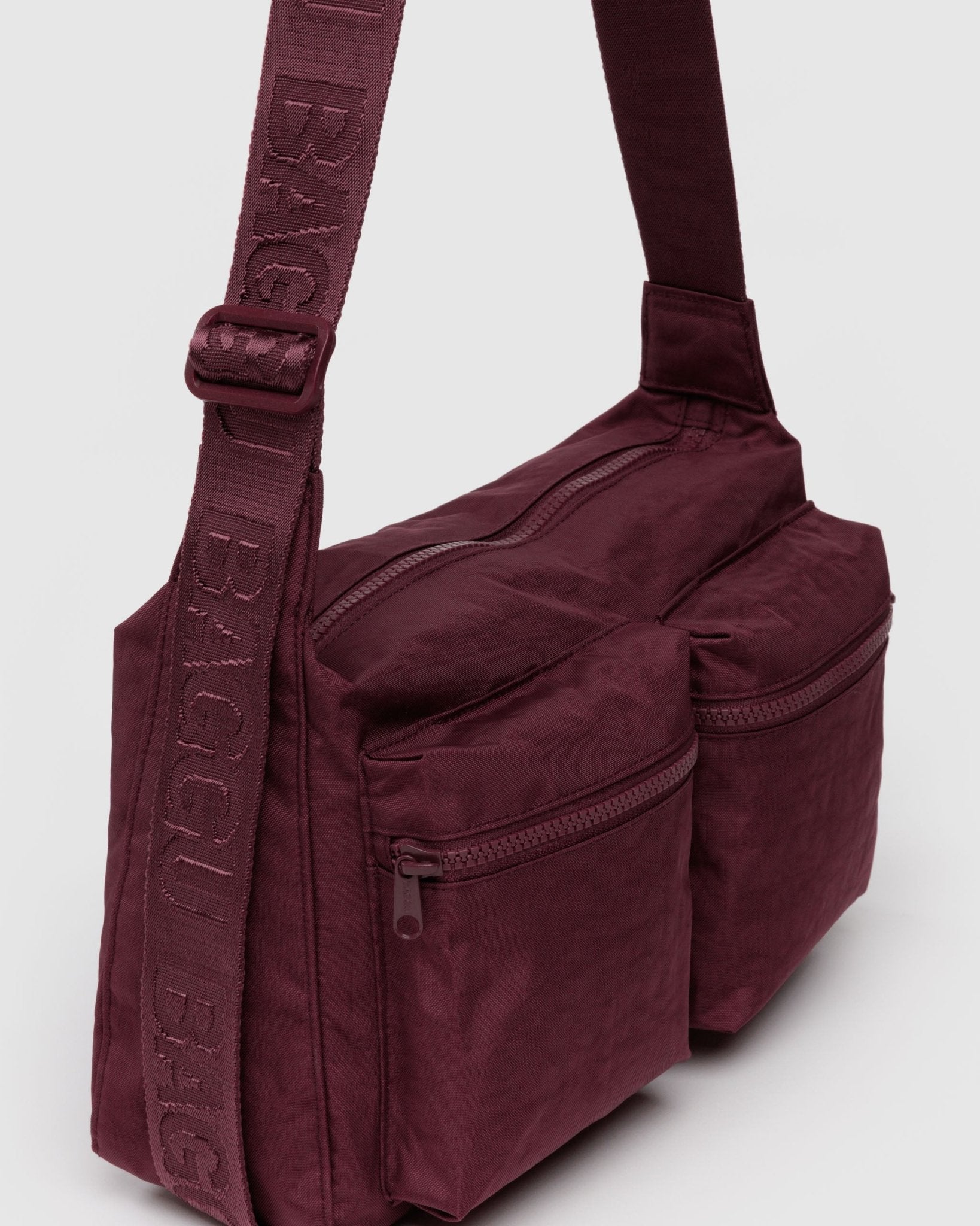 Maroon crossbody bag with visible branding on adjustable strap and two front zip pockets
