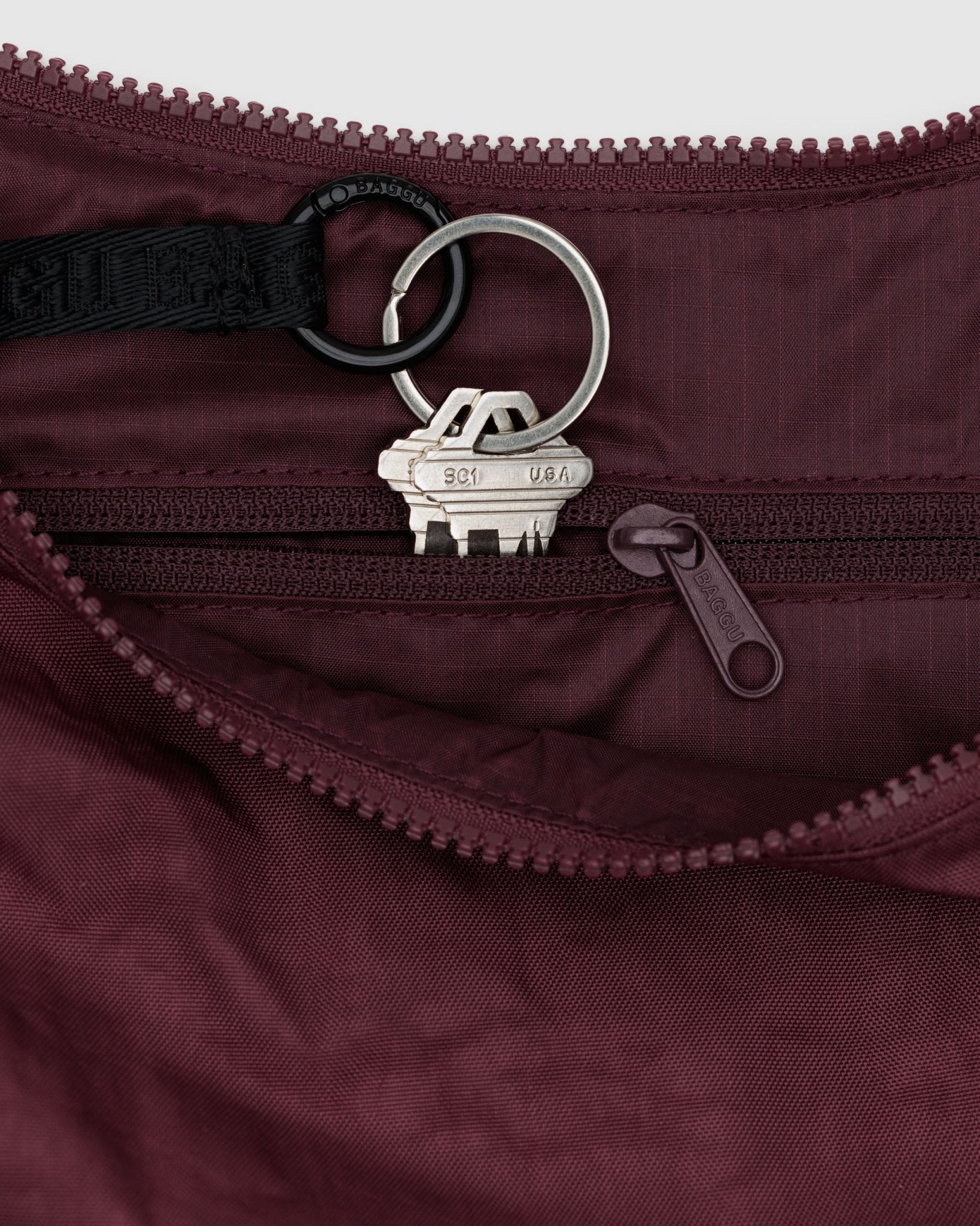 Close-up of a keychain with keys attached storing in an internal zip pocket of a maroon medium crescent bag