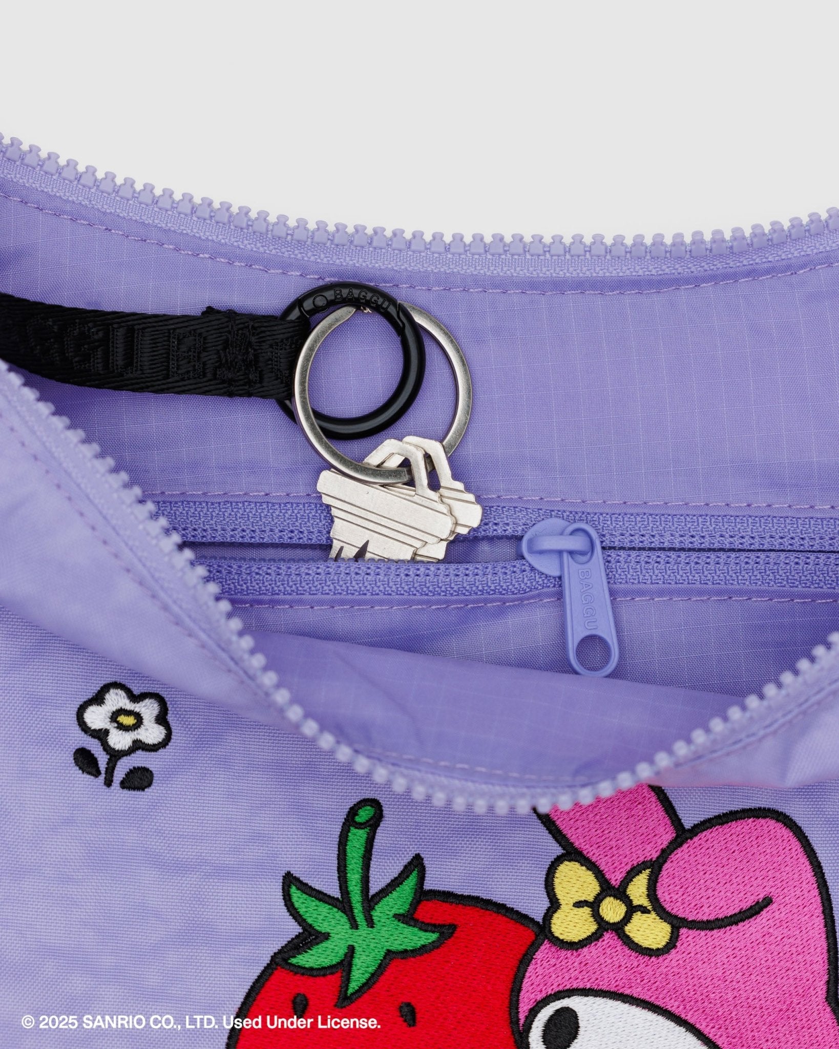 Close-up of a purple bag with key chain going into internal zip pouch, hello kitty and strawberry design on front