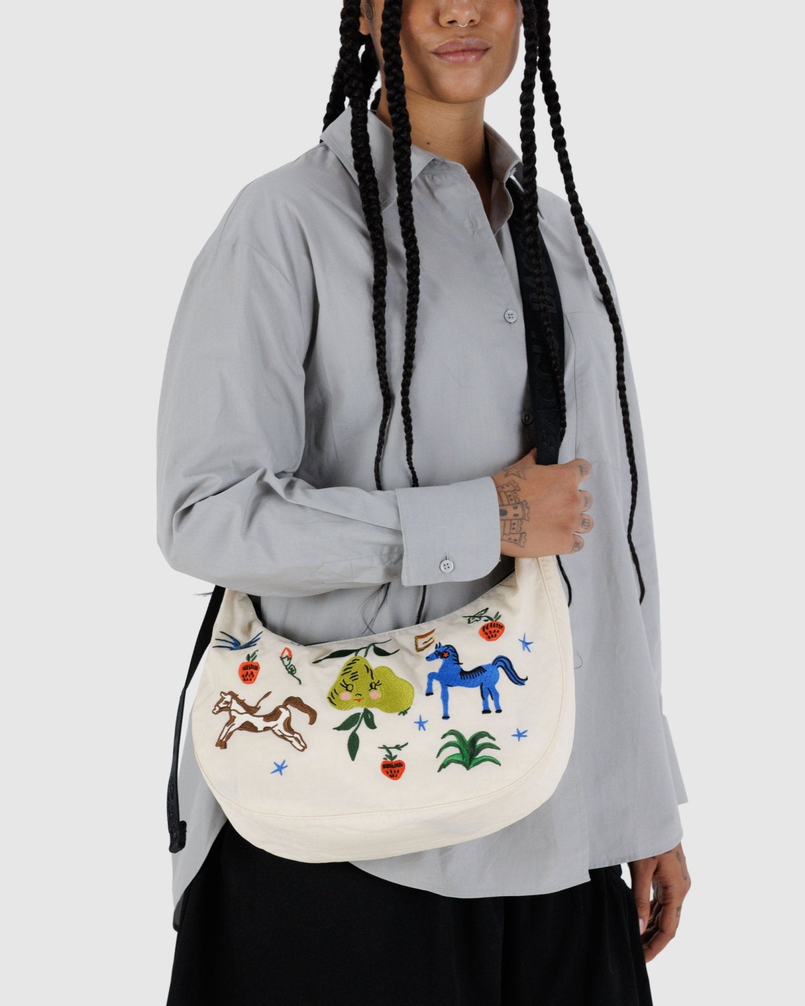 Person wearing a crossbody ecru medium crescent bag with horses and fruits print
