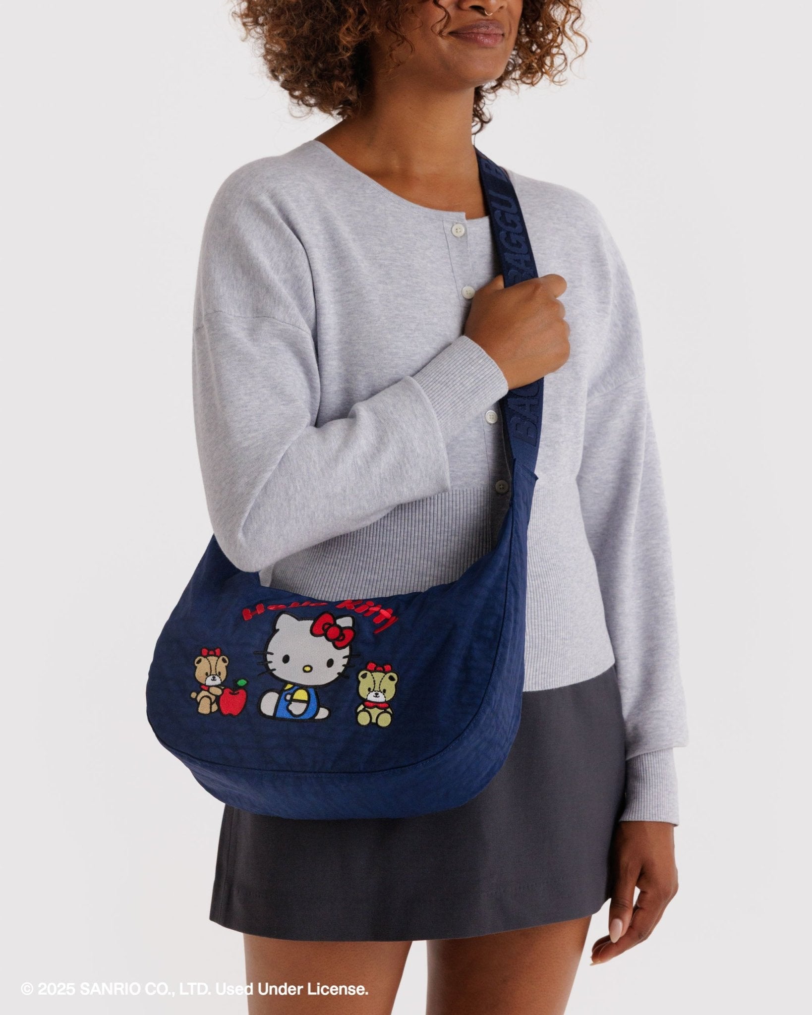 Person wearing a crossbody, blue bag with Hello Kitty and teddy design on front