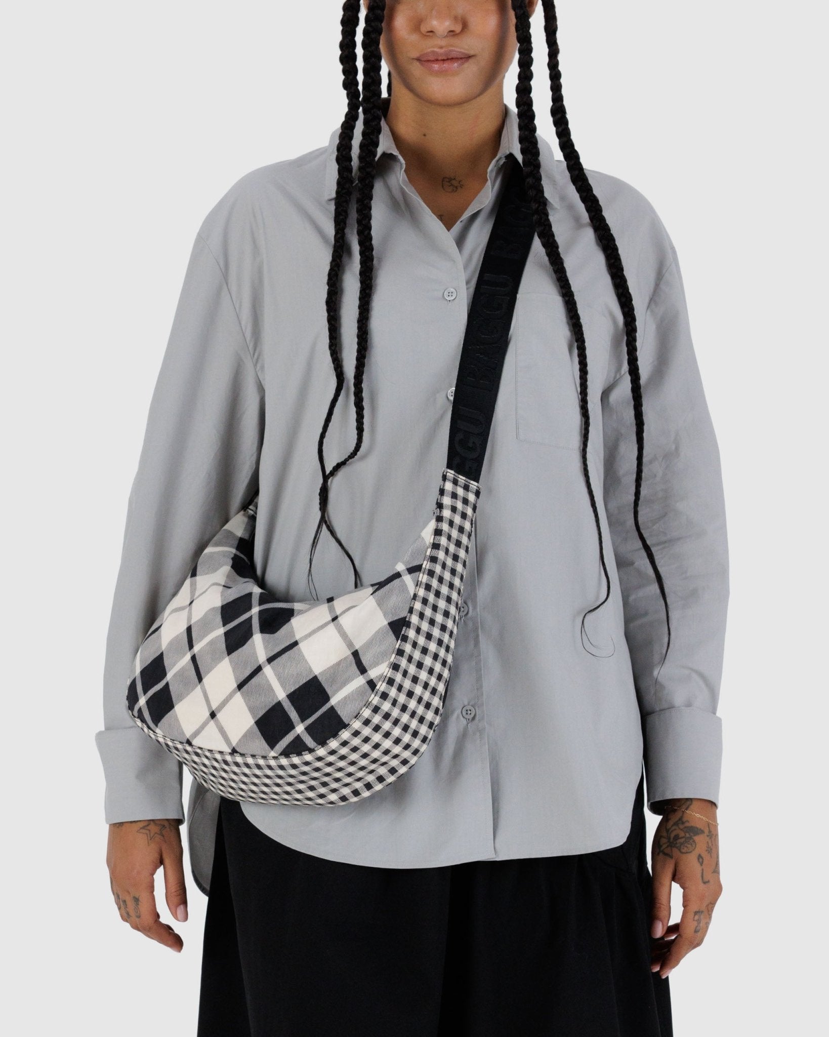 Person wearing a gray shirt with a mixed plaid crescent bag over one shoulder