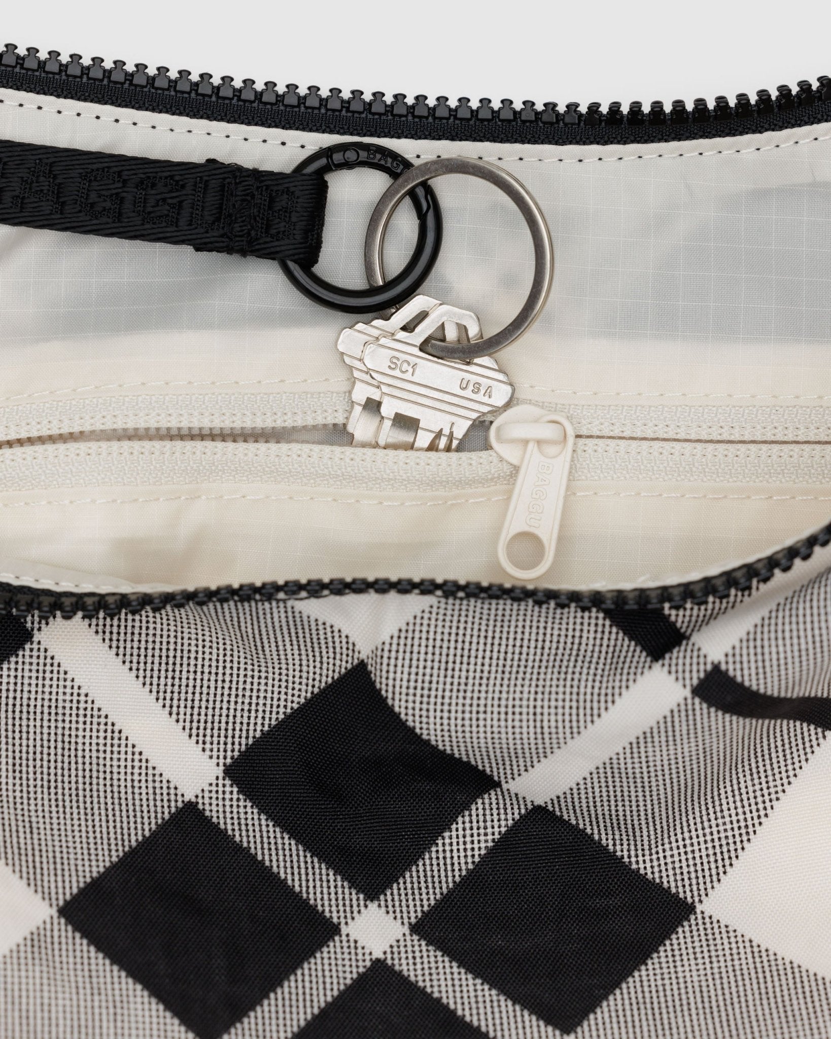Close-up of a mixed plaid crescent bag with a keychain going into internal zip pouch