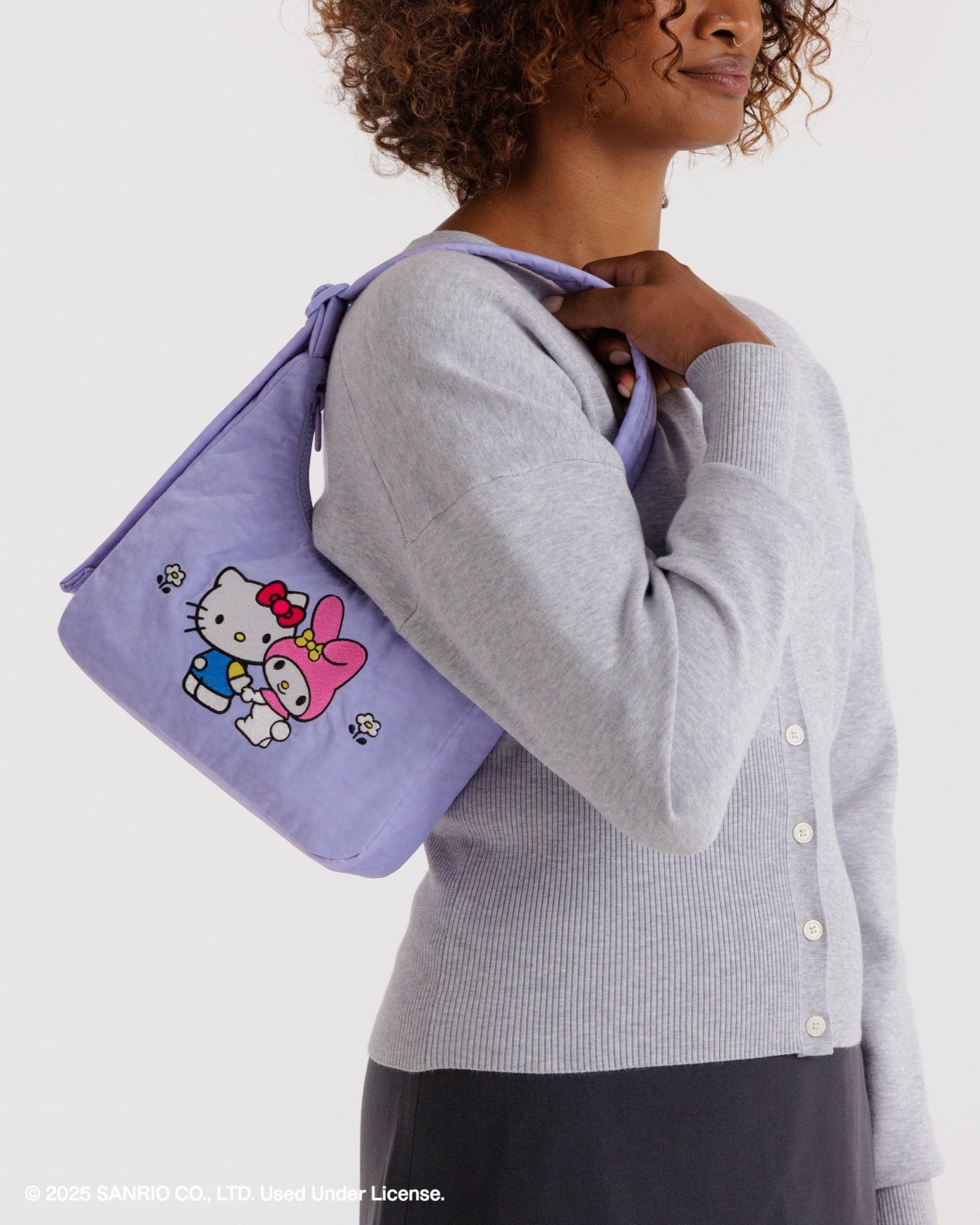 Person holding a mini purple shoulder bag with two Hello Kitty characters design on front over shoulder