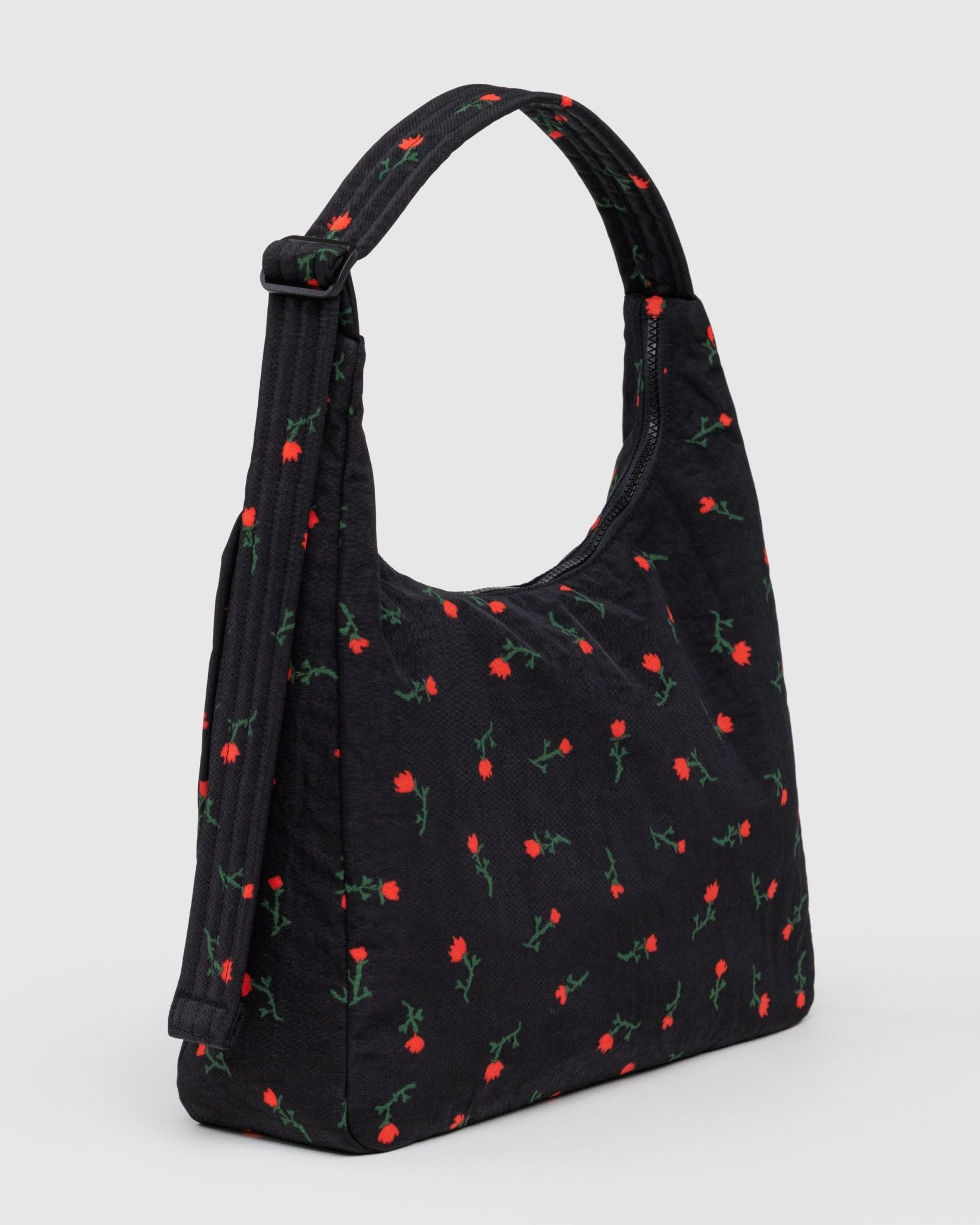 Black shoulder bag covered in red wildflower floral pattern with zip top closure and quilted adjustable shoulder strap