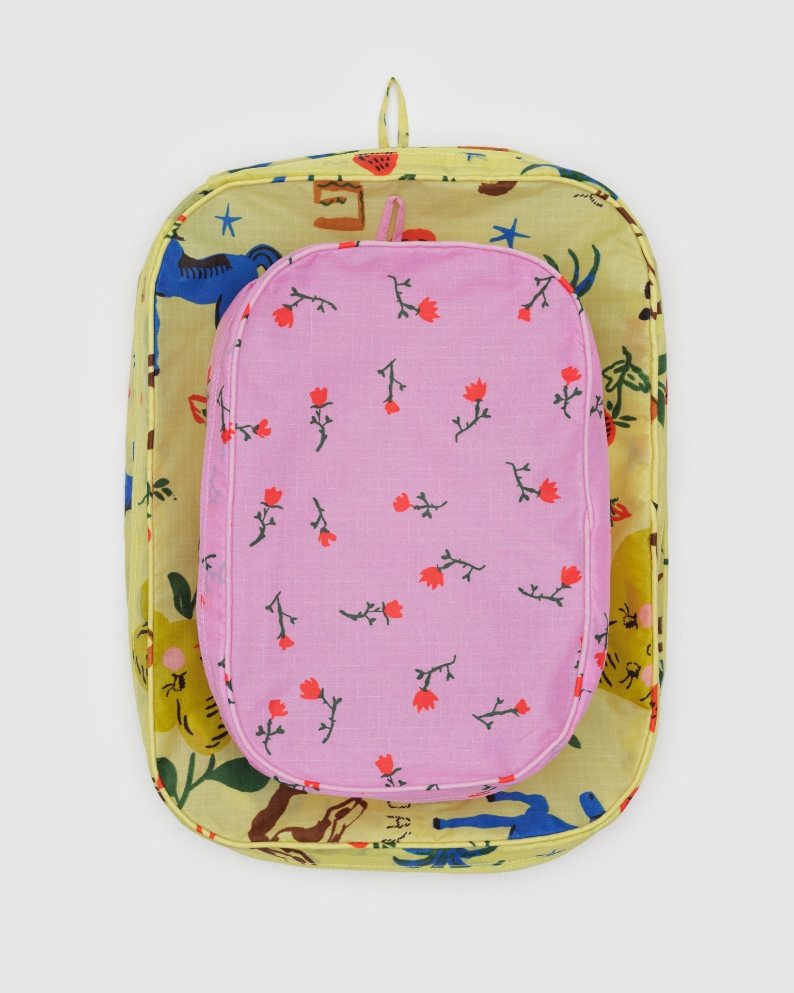 Two different sized packing cubes, one yellow with horse and fruit print and one pink with flowers print