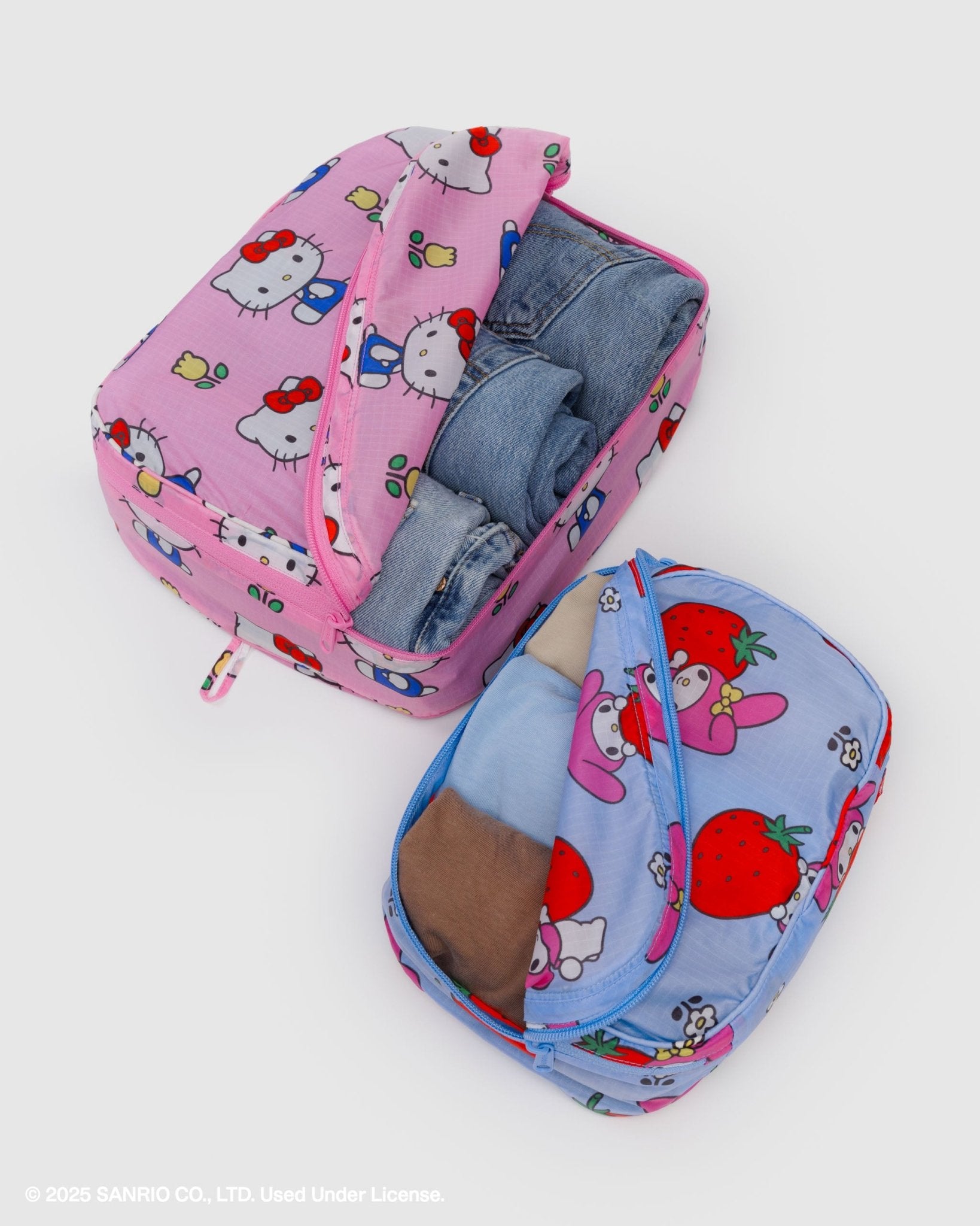 Two pink and blue packing cubes with hello kitty cartoon character prints and zip tops with clothes inside