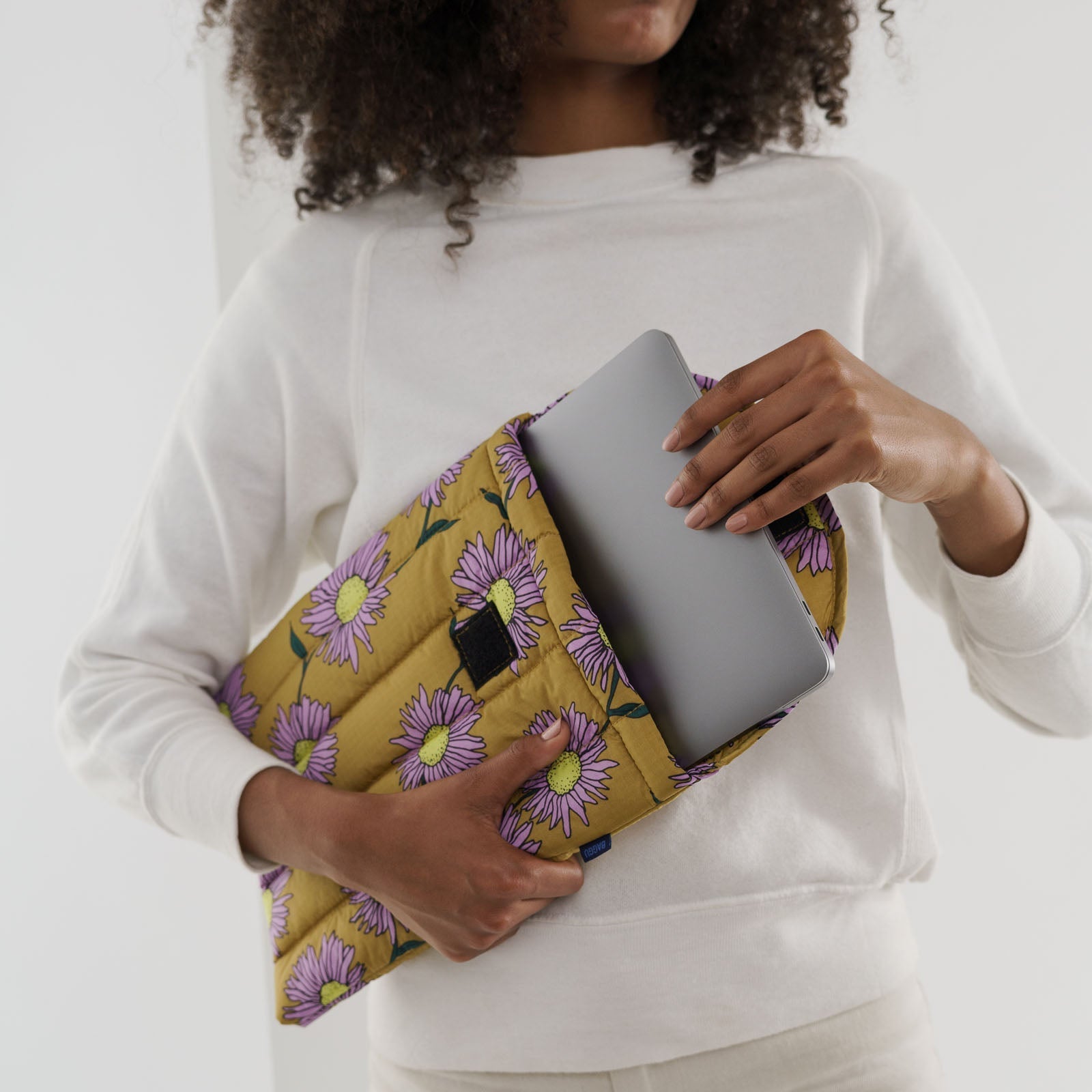 Person holding a yellow floral-patterned bag with a laptop inside