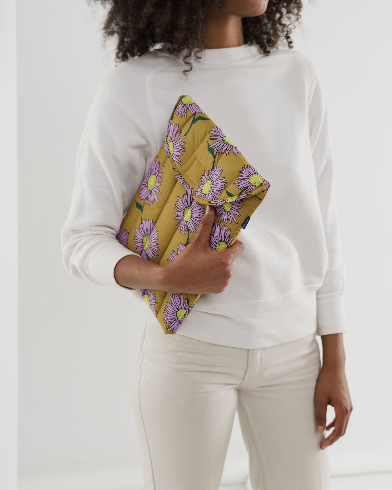 Person holding a yellow laptop sleeve with pink daisy flower pattern under arm