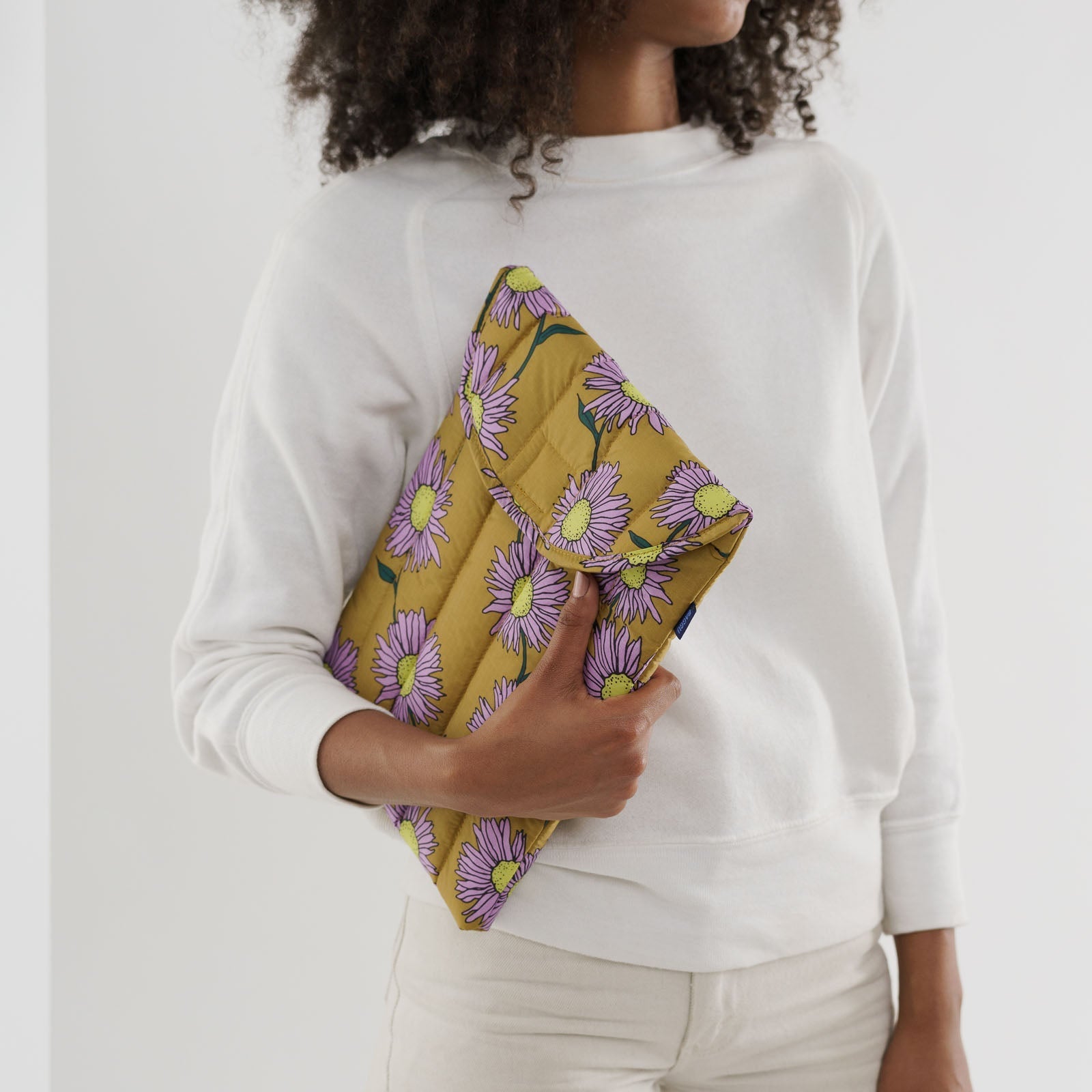Person holding a yellow laptop sleeve with pink daisy flower pattern under arm