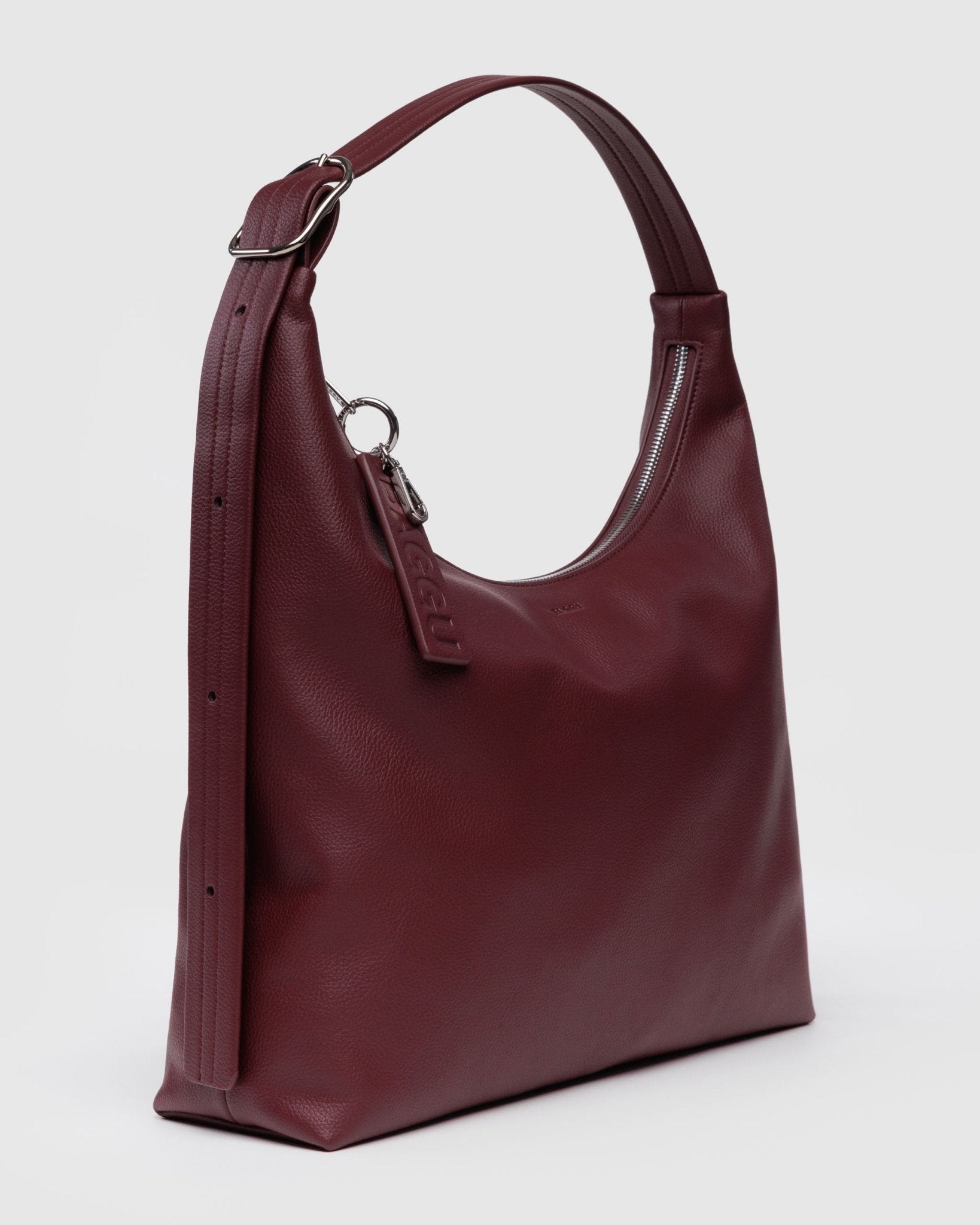 Side view of burgundy/maroon handbag with adjustable shoulder strap with silver hardware and zipper