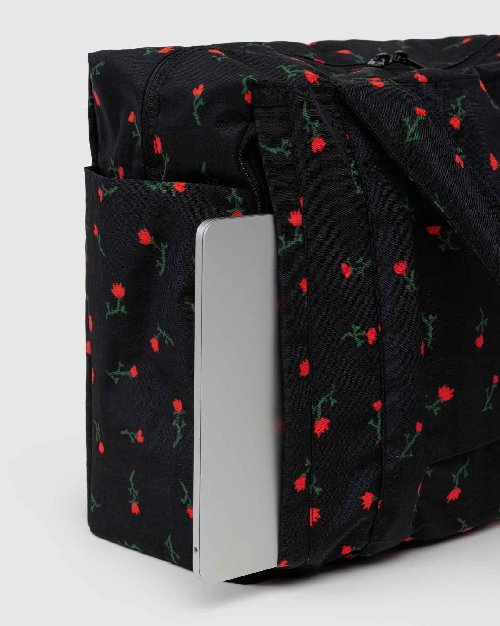 Small black duffel bag with red wildflower pattern and a silver laptop inside laptop zip pouch