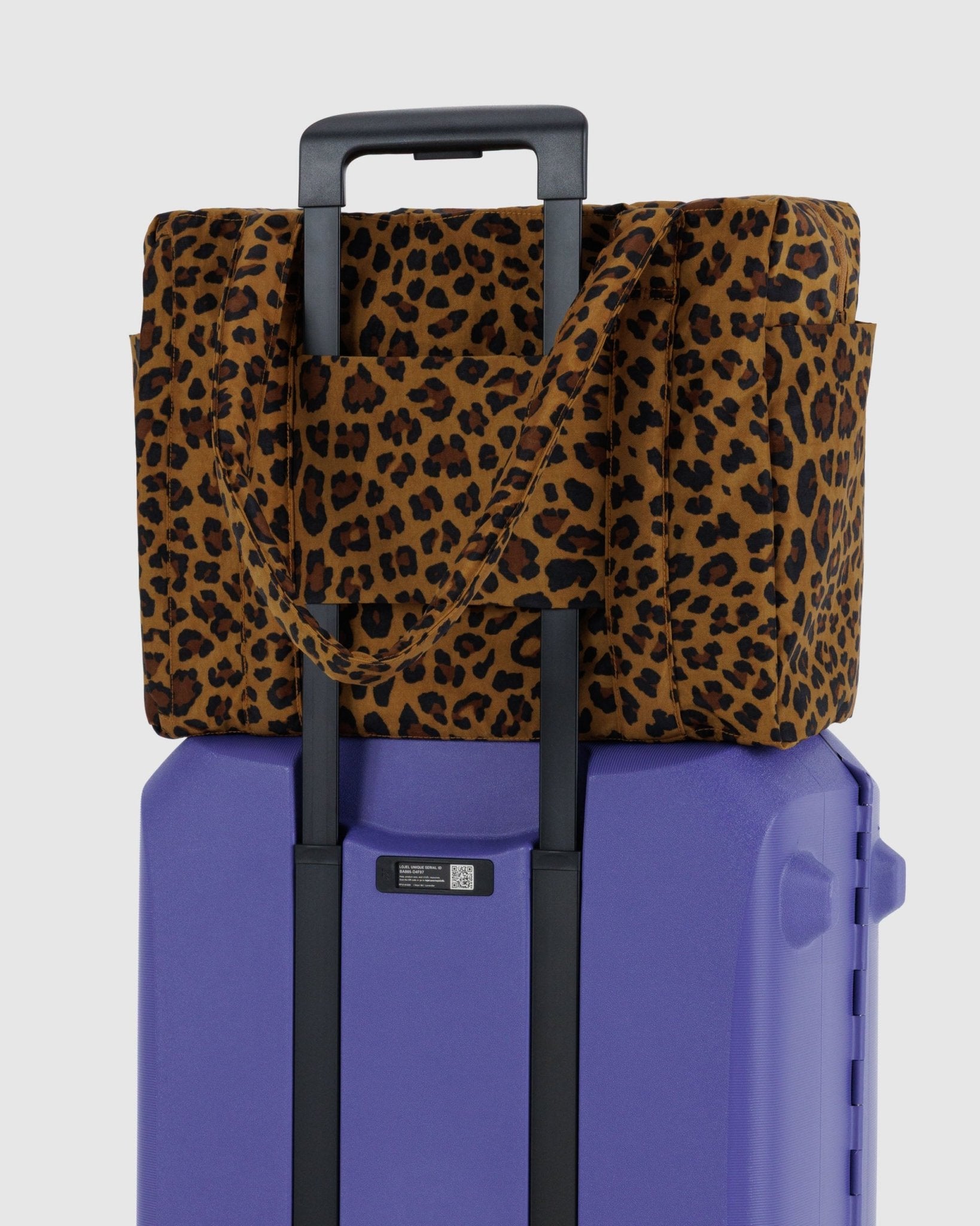 Baggu Small Cloud Carry On Leopard bag with travel sleeve attached to handle of purple suitcase