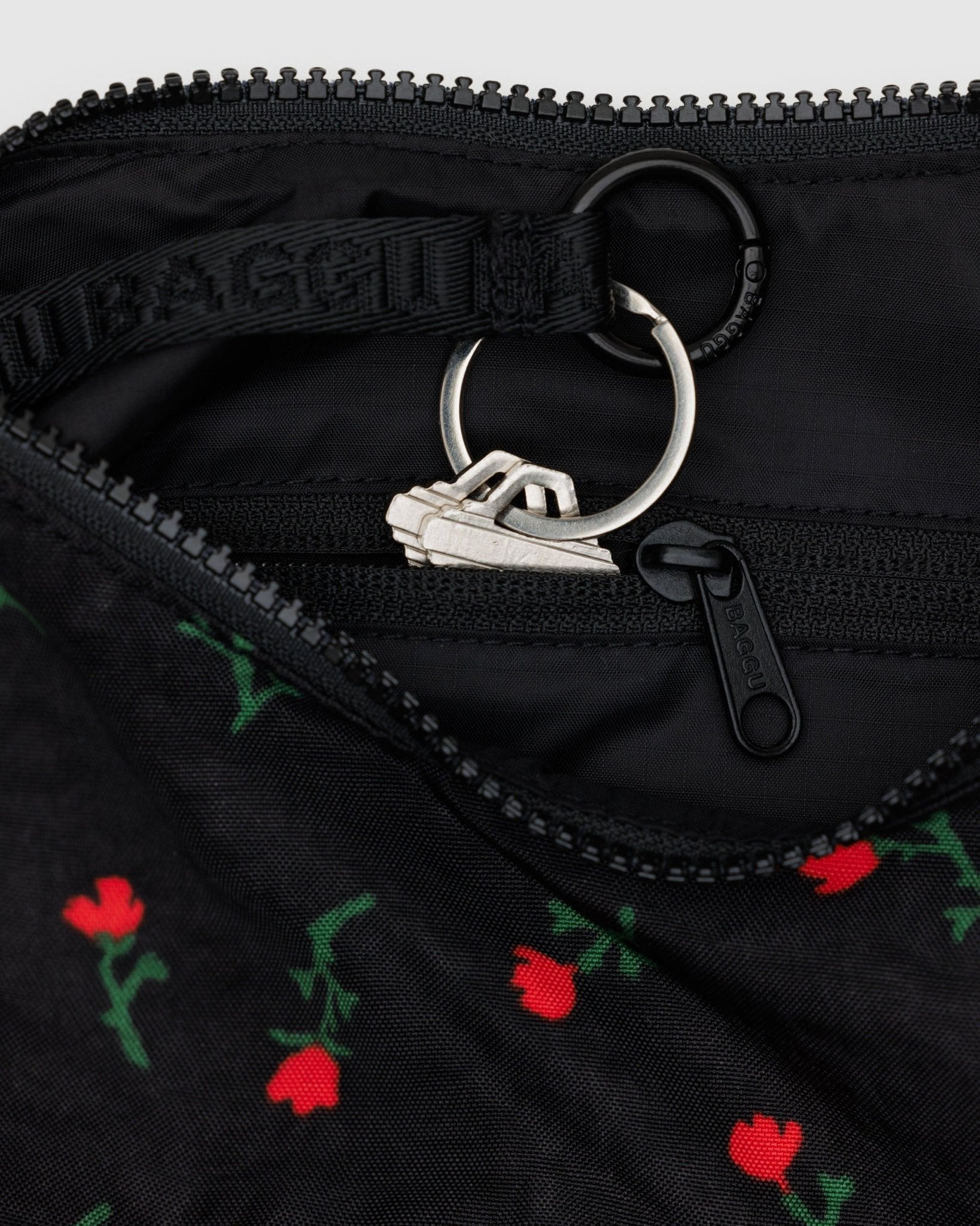 Small black bag with red wildflower pattern, zip top and a keychain attached, featuring the brand 'BAGGU'.