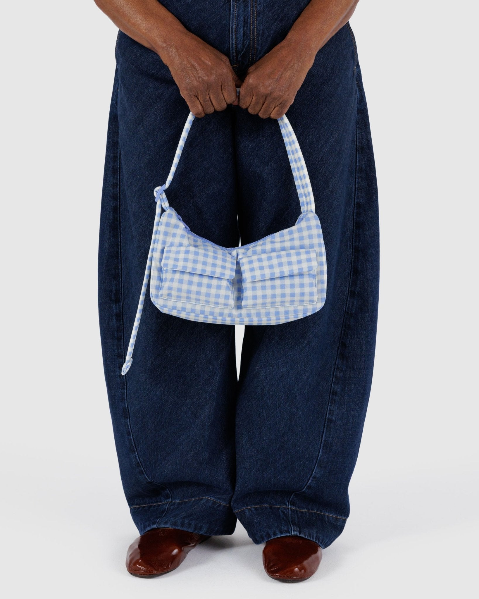 Woman holding a light blue gingham cargo shoulder bag by quilted adjustable strap.