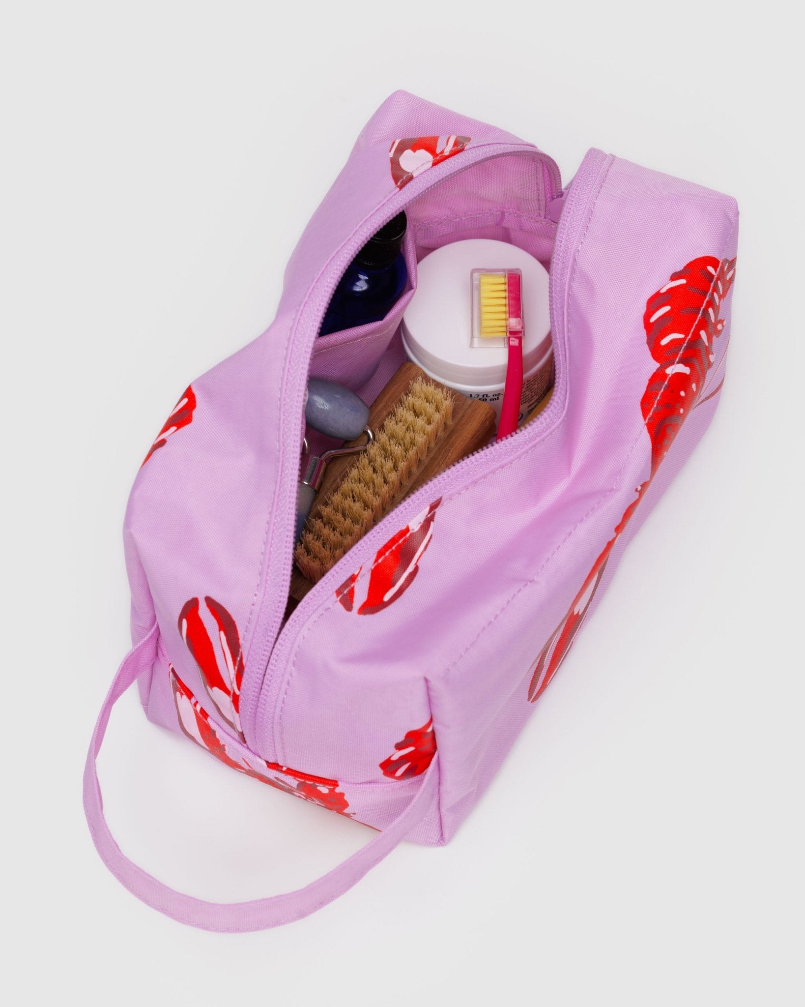 Pink toiletry bag with red lobster patterns containing various bathroom items.