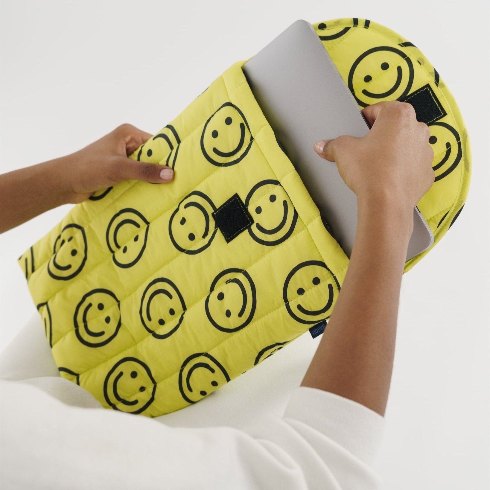 person taking laptop out of quilted yellow smiley face print carry case.