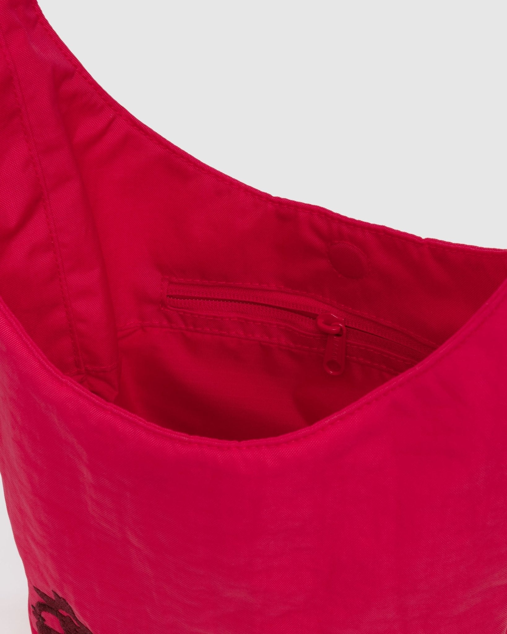 Close-up of a red sling bag with an internal zipper pocket and magnetic top closure