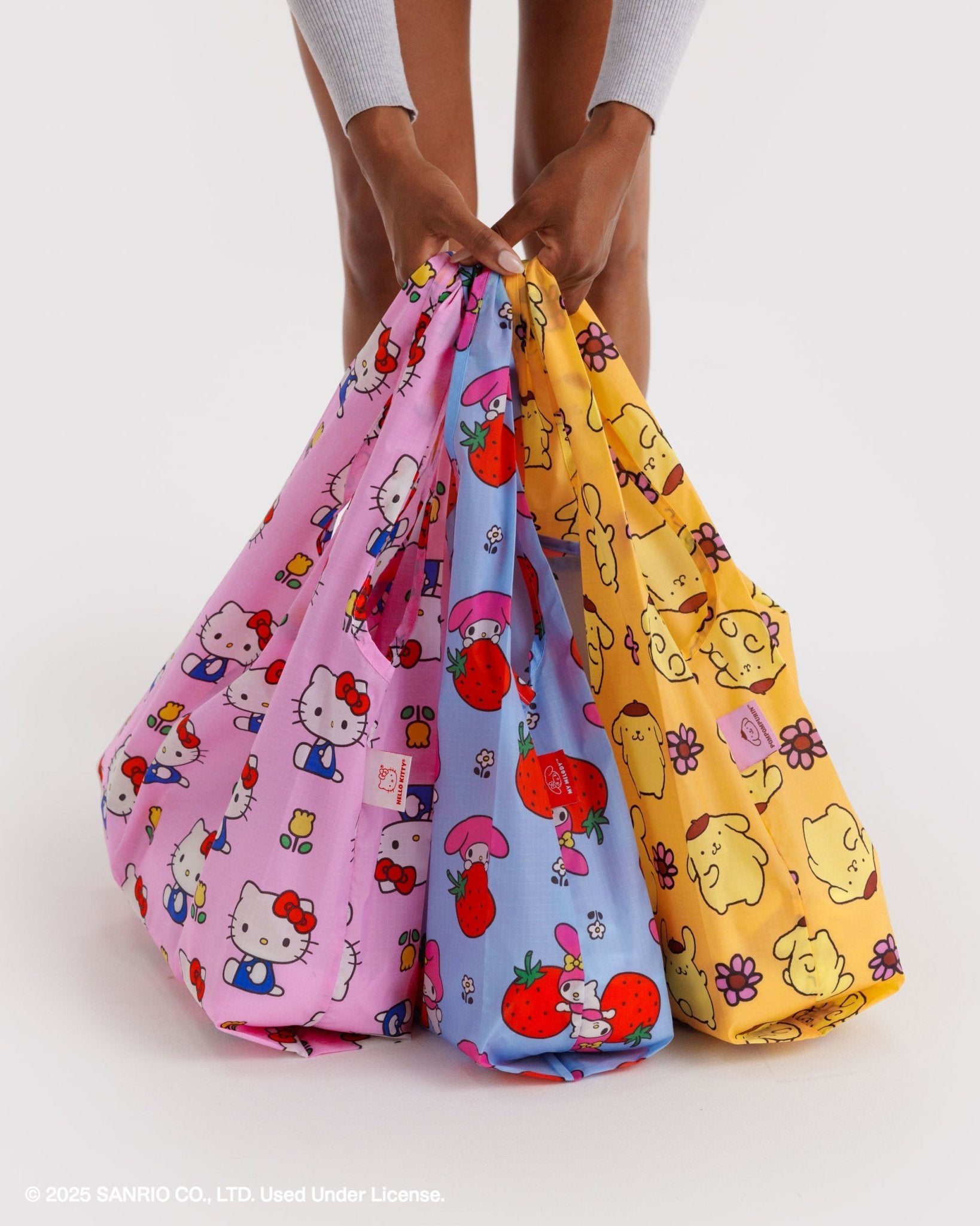 Three standard sized colourful bags with hello kitty characters print held by a person