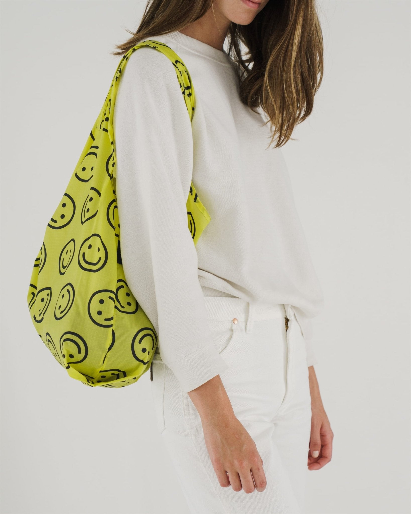 Side view of a woman in white garments wearing a yellow and smiley face print bag over shoulder.