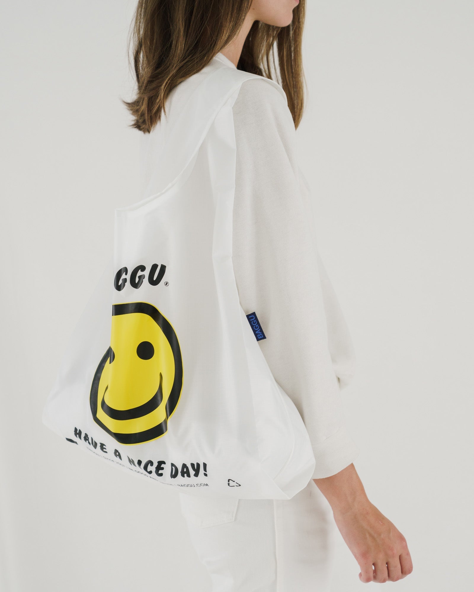 Person holding a yellow smiley face Standard Baggu Reusable Bag on shoulder - ANNIE.G
