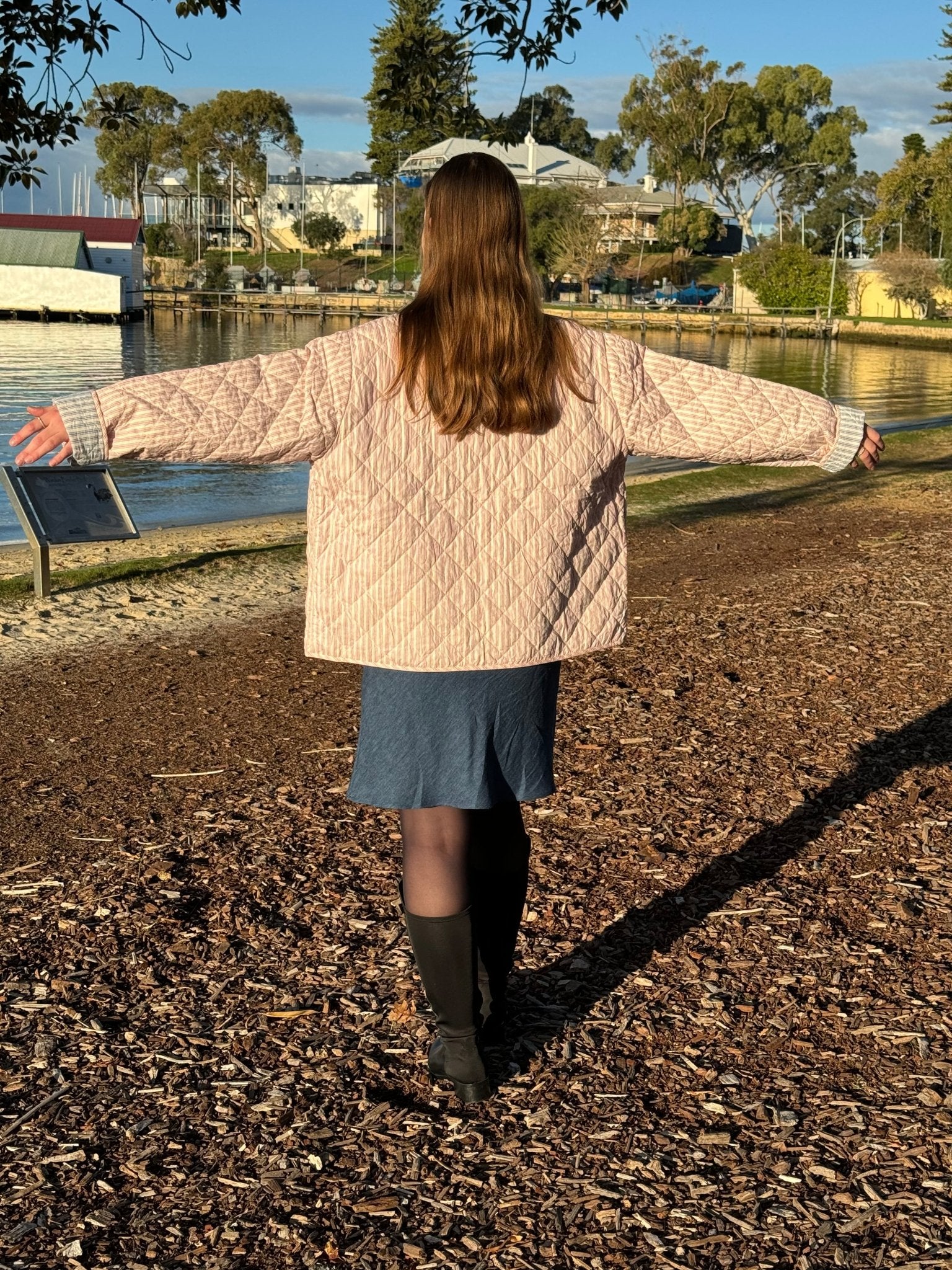 Back of woman wearing a blue Bias Slip Mini Dress and pink stripe quilted jacket with arms out to the side.