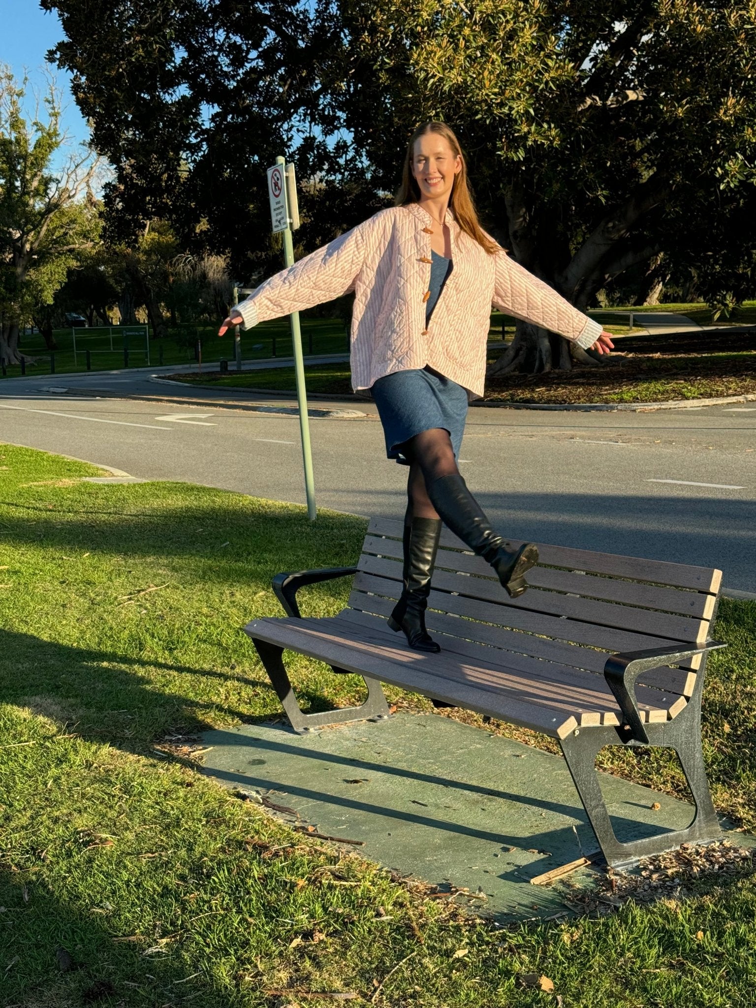 Woman wearing a blue denim Bias Slip Mini Dress and pink stripe quilted jacket standing on a bench seat.