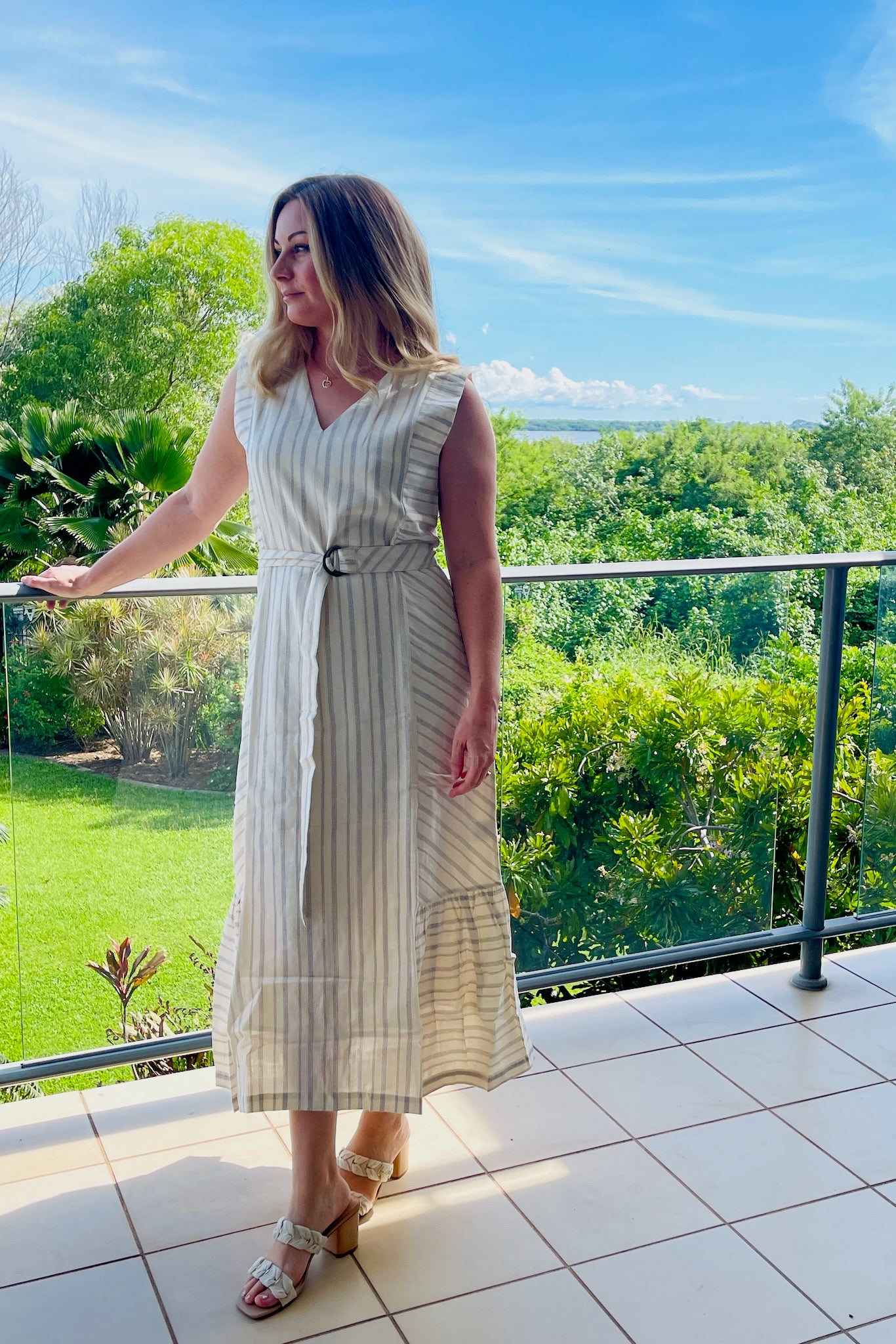 woman-wearing-cream-and-indigo-striped-sleeveless-dress-with-belt-standing-on-balcony-front-view