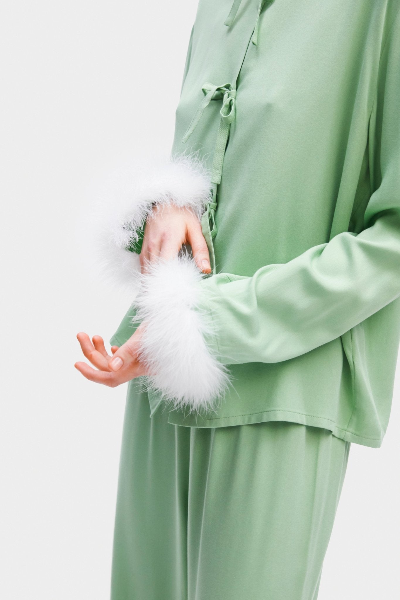 Close up of a person wearing pyjama top and pants touching white feather cuff on top - ANNIE.G