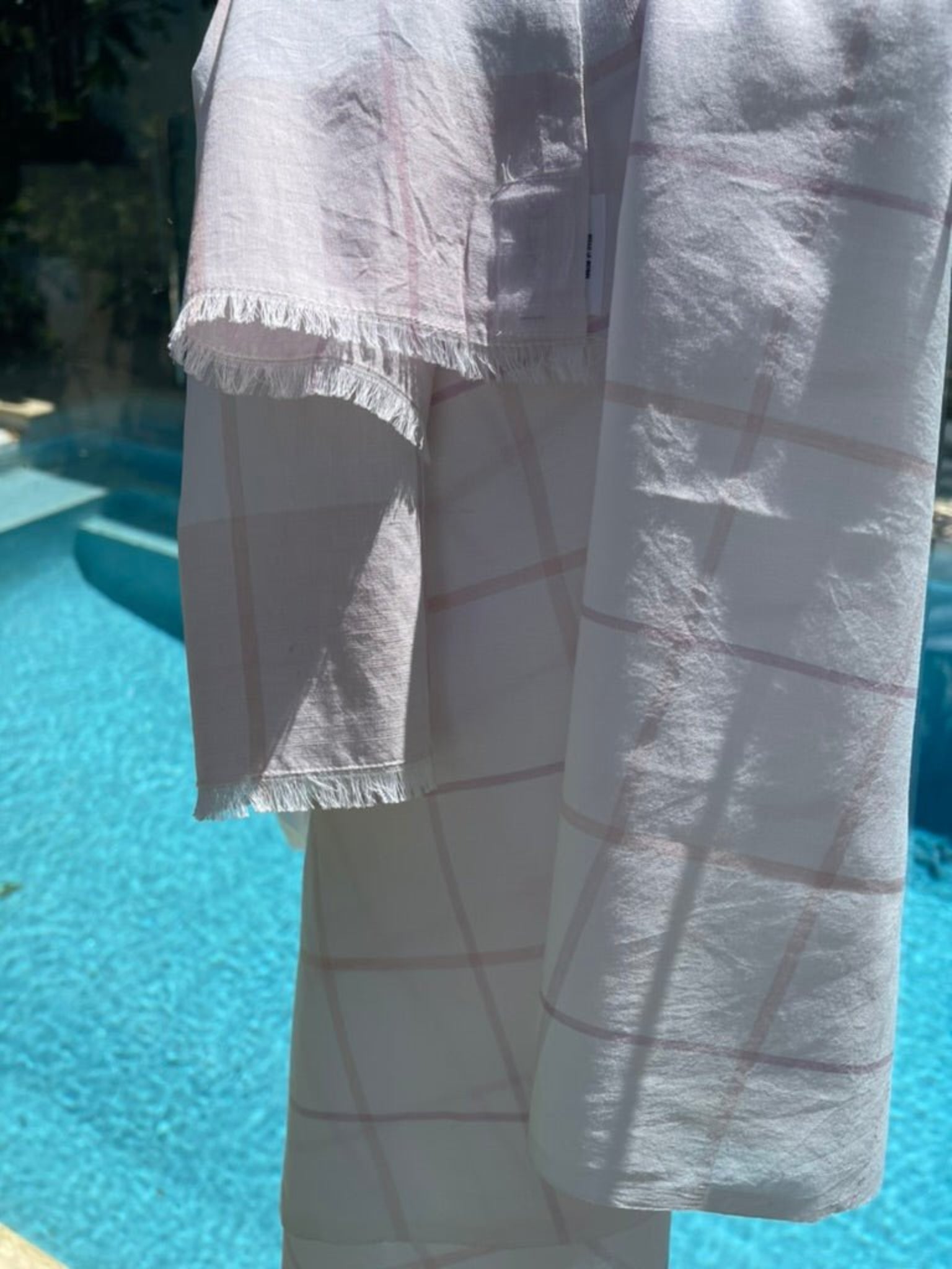 Pink and white check sarong with fringe thrown over glass pool fence - ANNIE.G