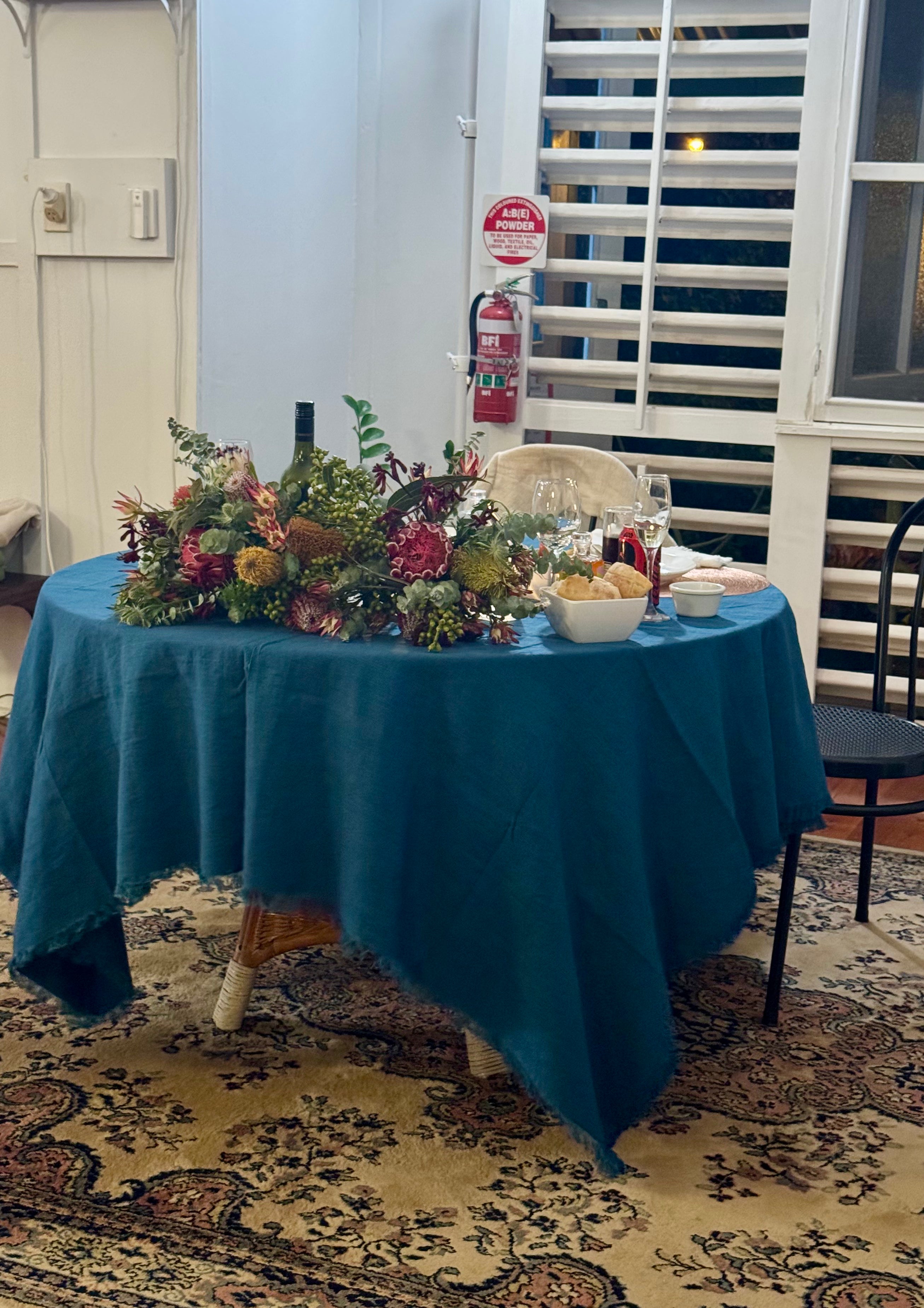 Round table set with a teal tablecloth, floral arrangement, and wine glasses at a wedding
