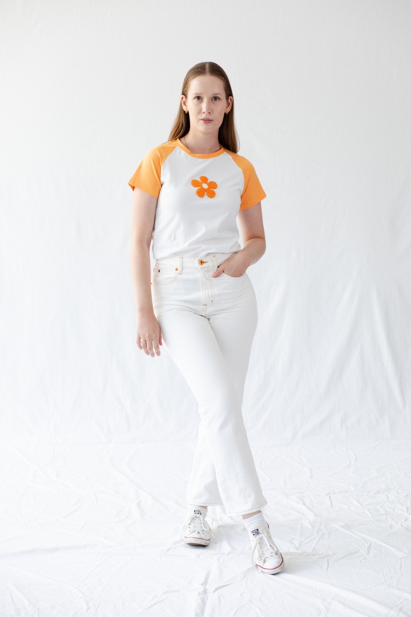 Woman wearing a white t-shirt with orange daisy on front and short orange sleeves with white jeans - ANNIE.G