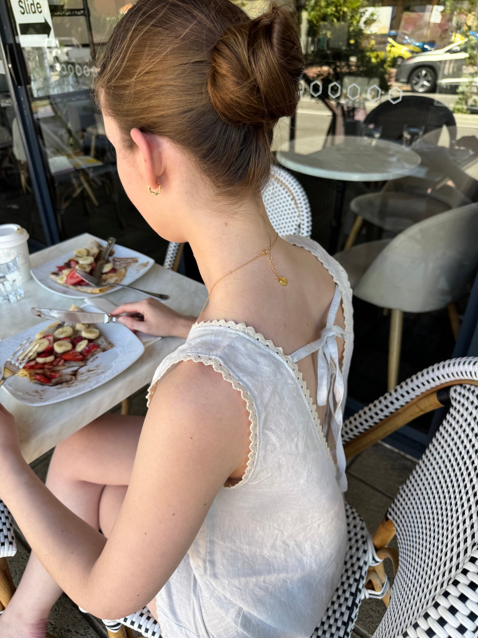 Woman in a light blue playsuit with ties at the back sitting at an outdoor table with food.