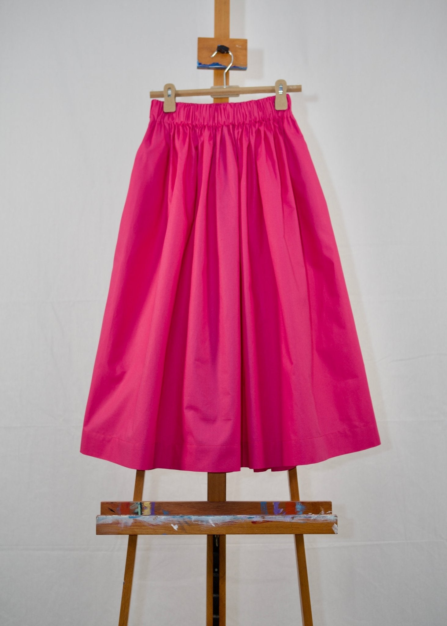 Hot pink gathered waist skirt in Italian cotton with elastic waistband hanging on a hanger on an easel - ANNIE.G