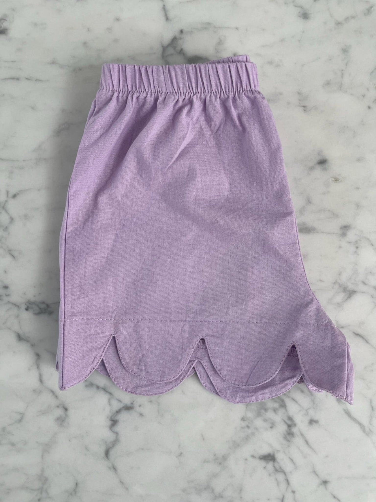 Purple shorts with curved hem folded in half on a bench - ANNIE.G