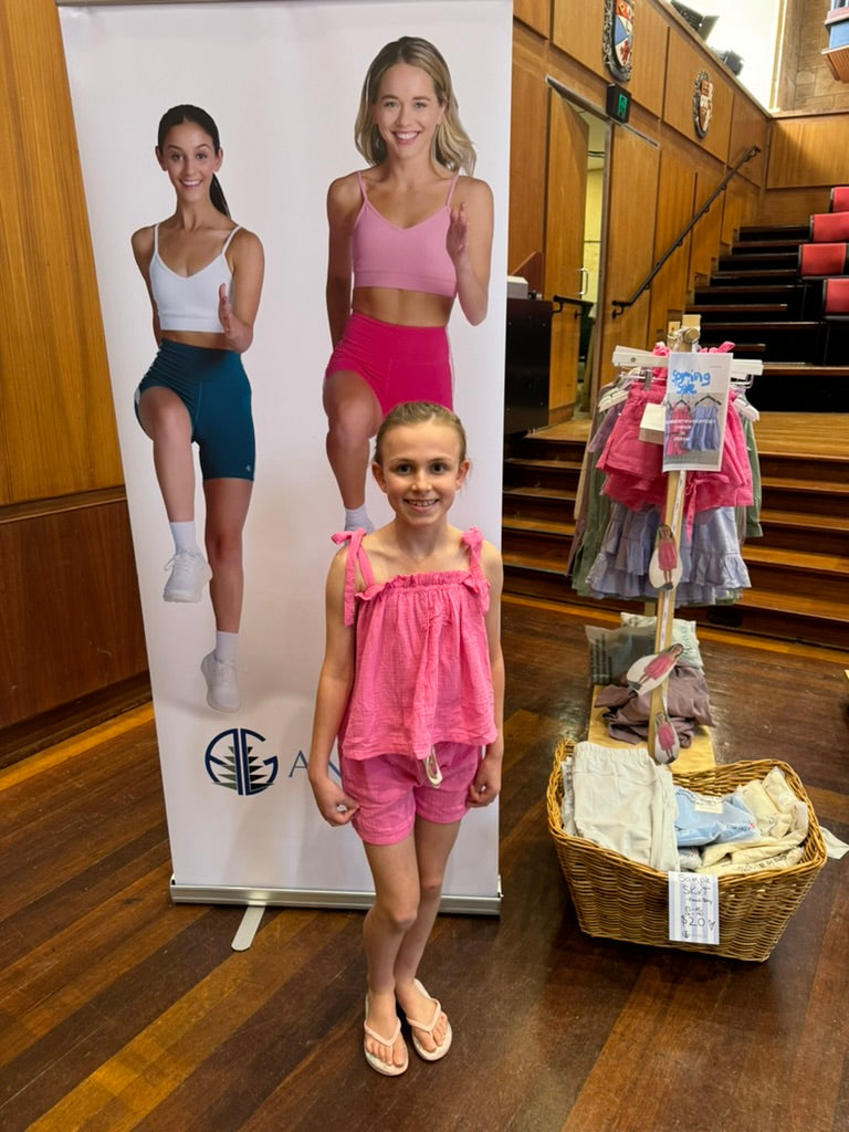 Young girl in pink top and shirts standing next to a display with cutout models in a market.