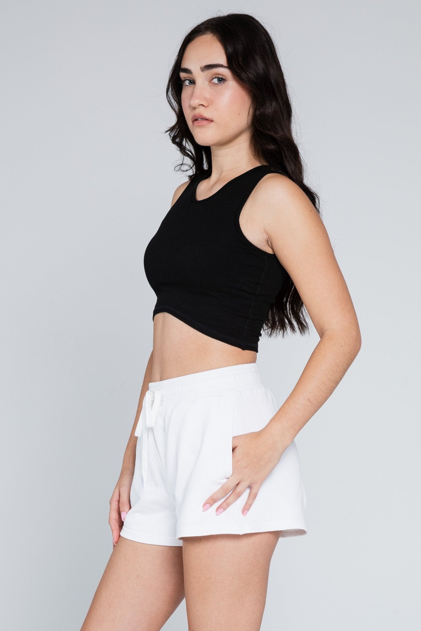 Woman wearing white Monterey Sweat Shorts with elastic waist and hands in pockets and black curved crop top - ANNIE.G