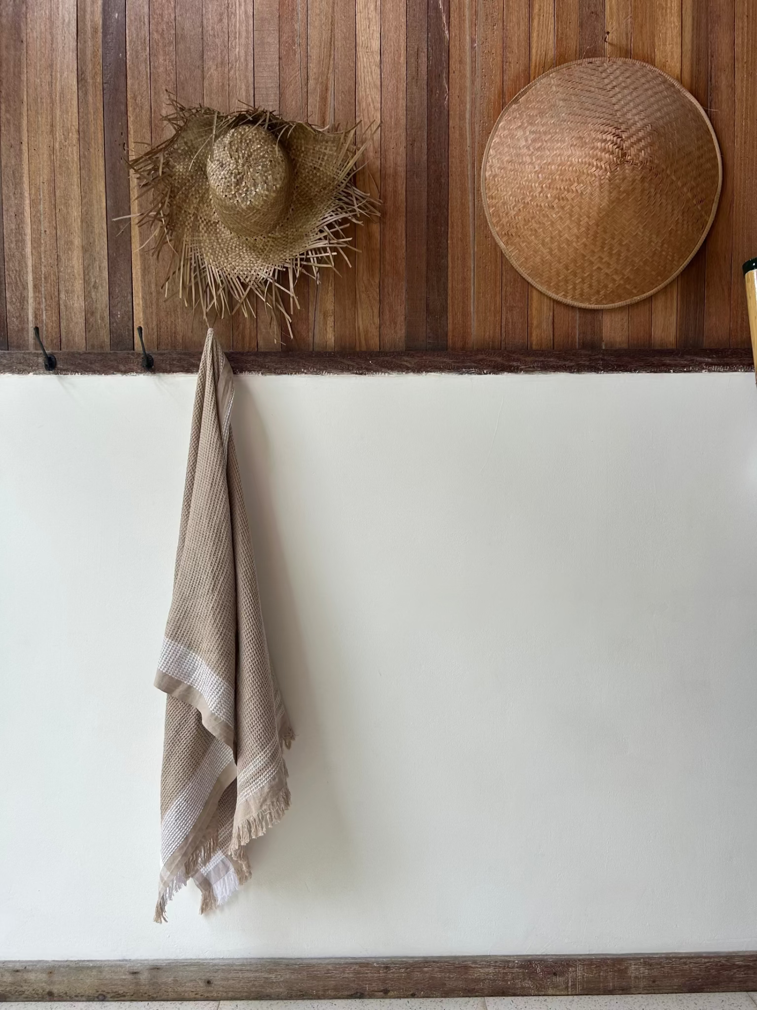 Two straw hats and a natural waffle towel hanging on a wooden wall.