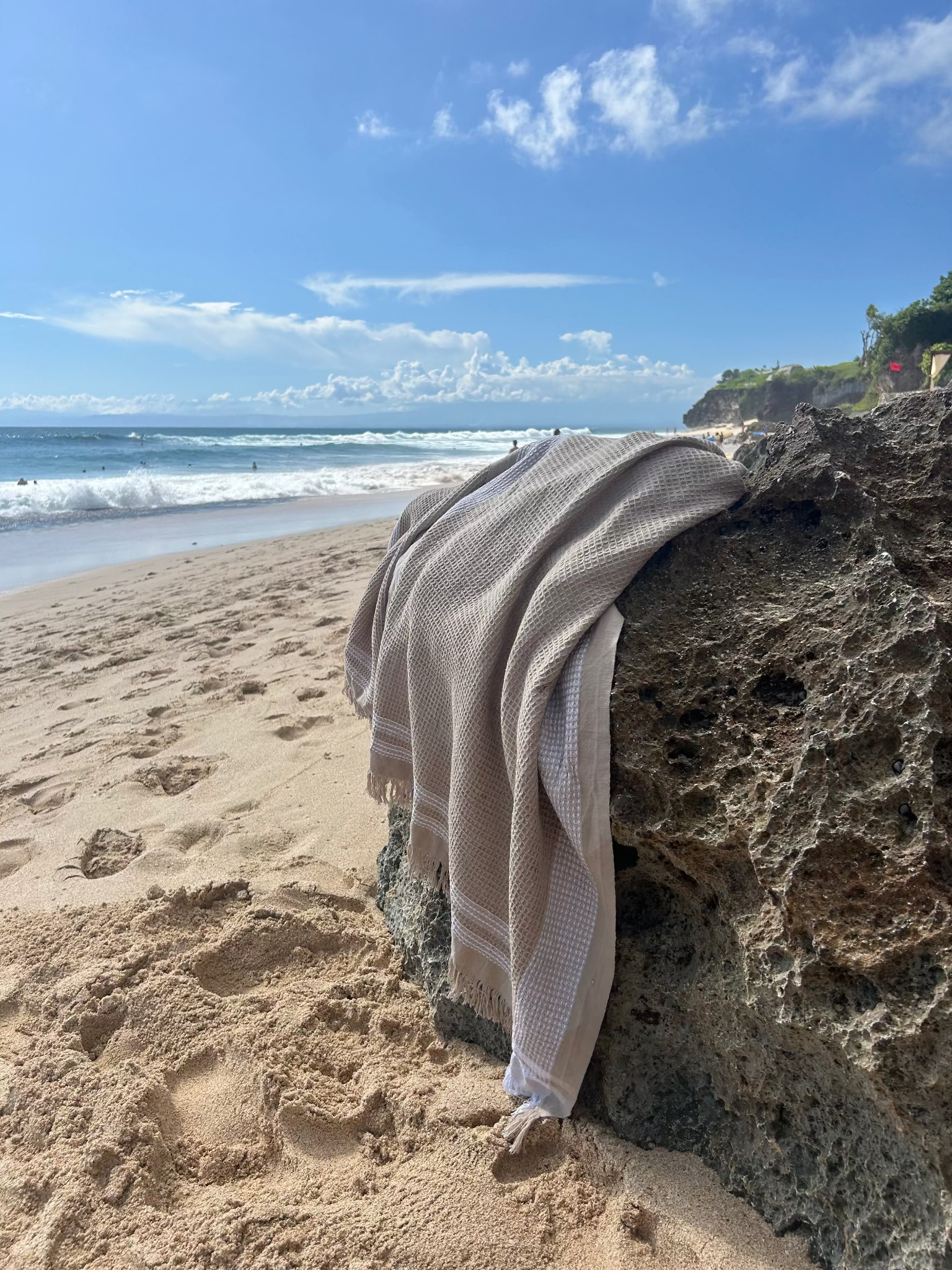 Waffle towel draped over a rock on a sandy beach with ocean and sky in the background.