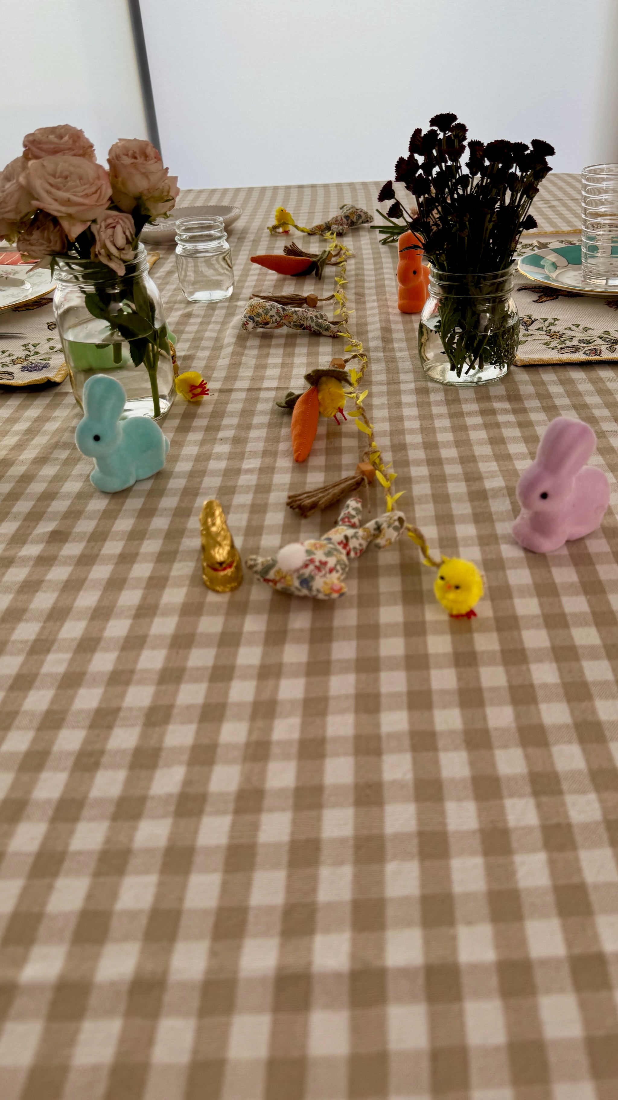bone-and-white-gingham-patterned-tablecloth-on-table-with-easter-decorations-flower-vases-and-place-settings