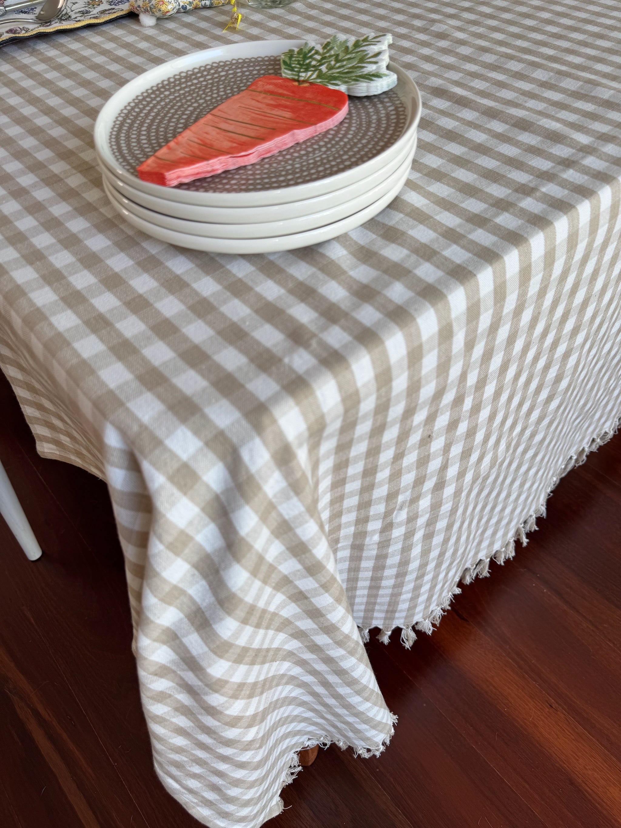 natural-gingham-tablecloth-hand-knotted-edge-laid-on-table-plates-and-serviettes-stacked-on-top