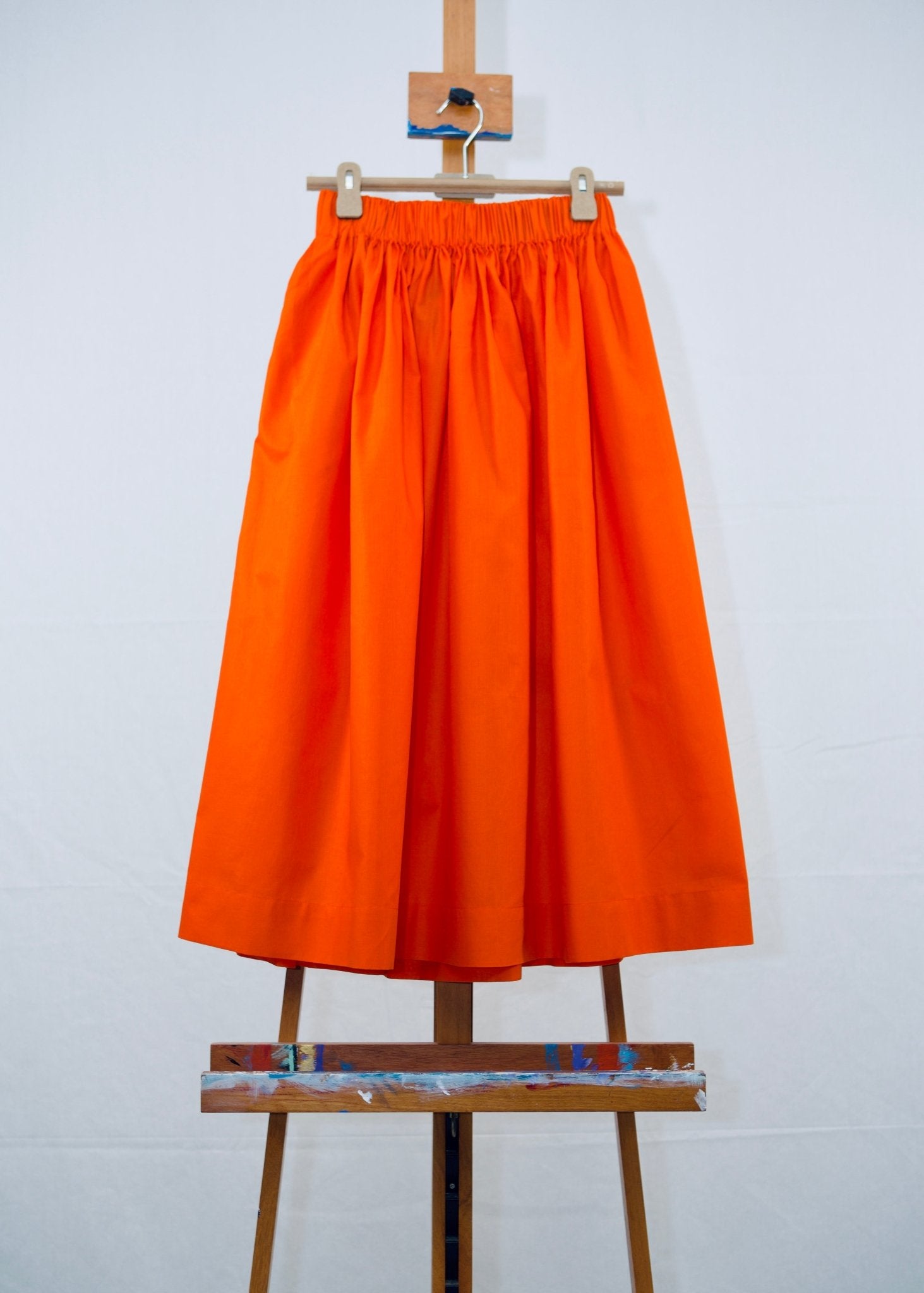 Orange Gathered Waist Skirt hanging on a hanger on a painting easel - ANNIE.G