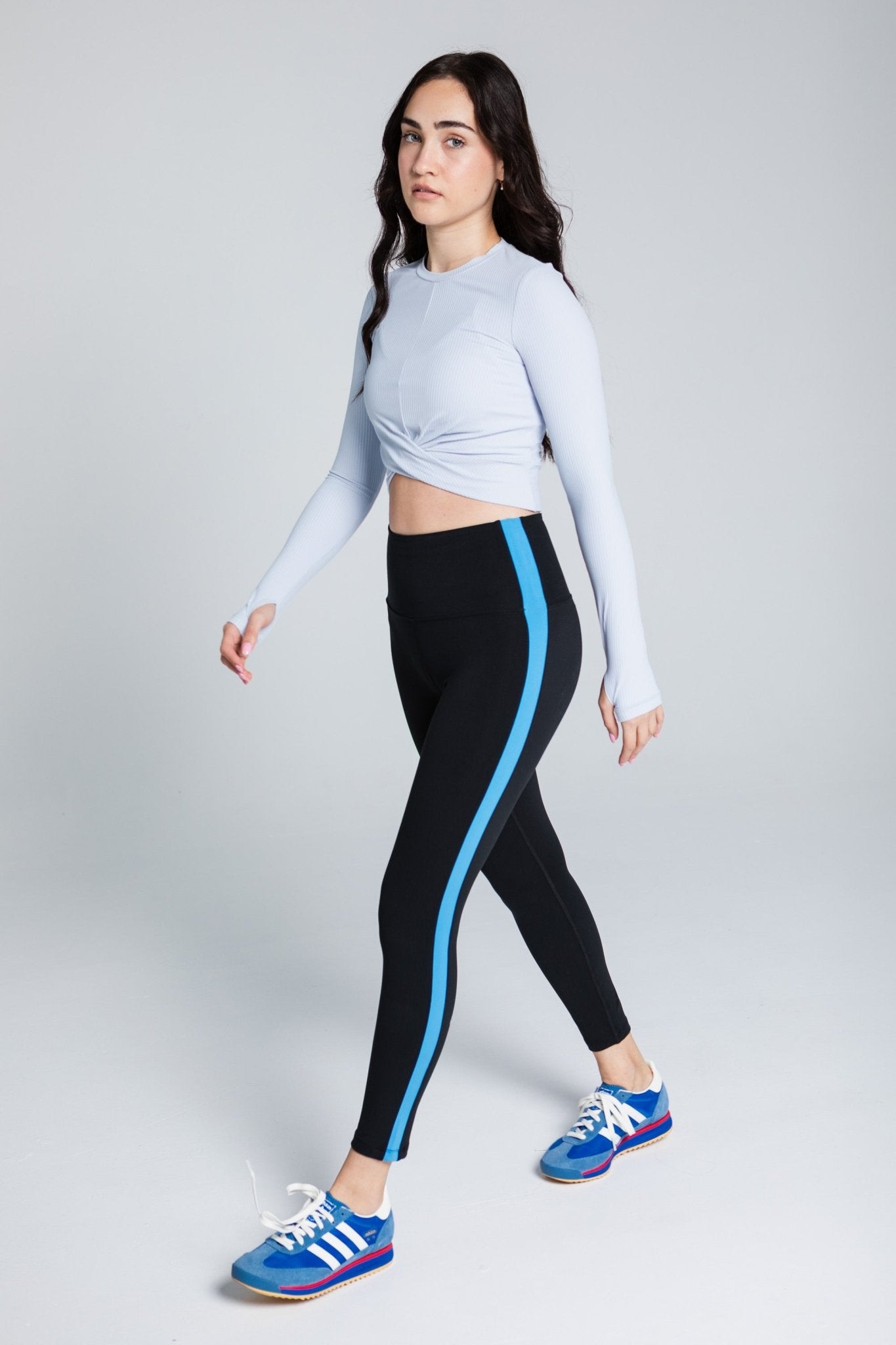 Woman wearing 3/4 black legging with blue side stripe and blue wrap top with long sleeves and thumb holes.