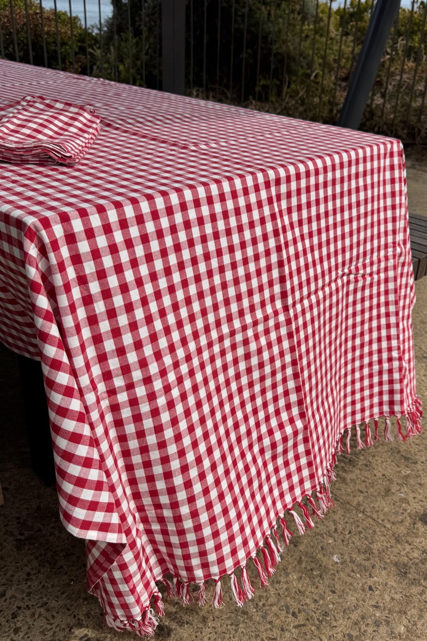 Red Gingham Cotton Tablecloth with hand knotted fringe and stack of napkins on a bbq table - ANNIE.G